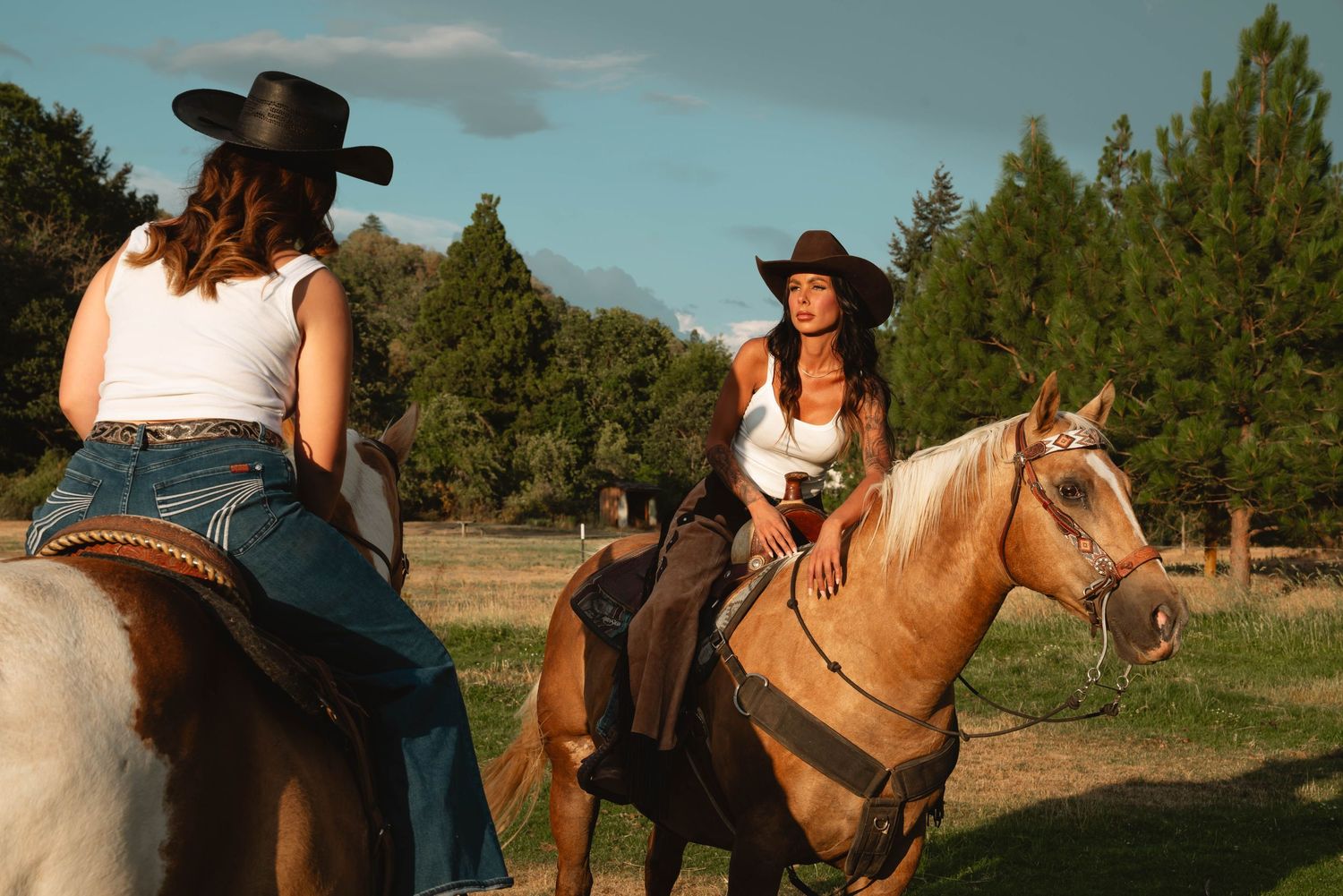 Two horses and riders traverse a scenic mountain trail during sunset.