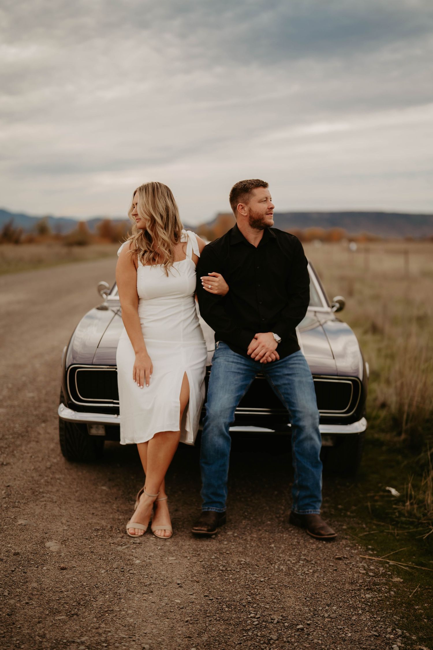 Couple sitting on classic car hood against desert landscape.