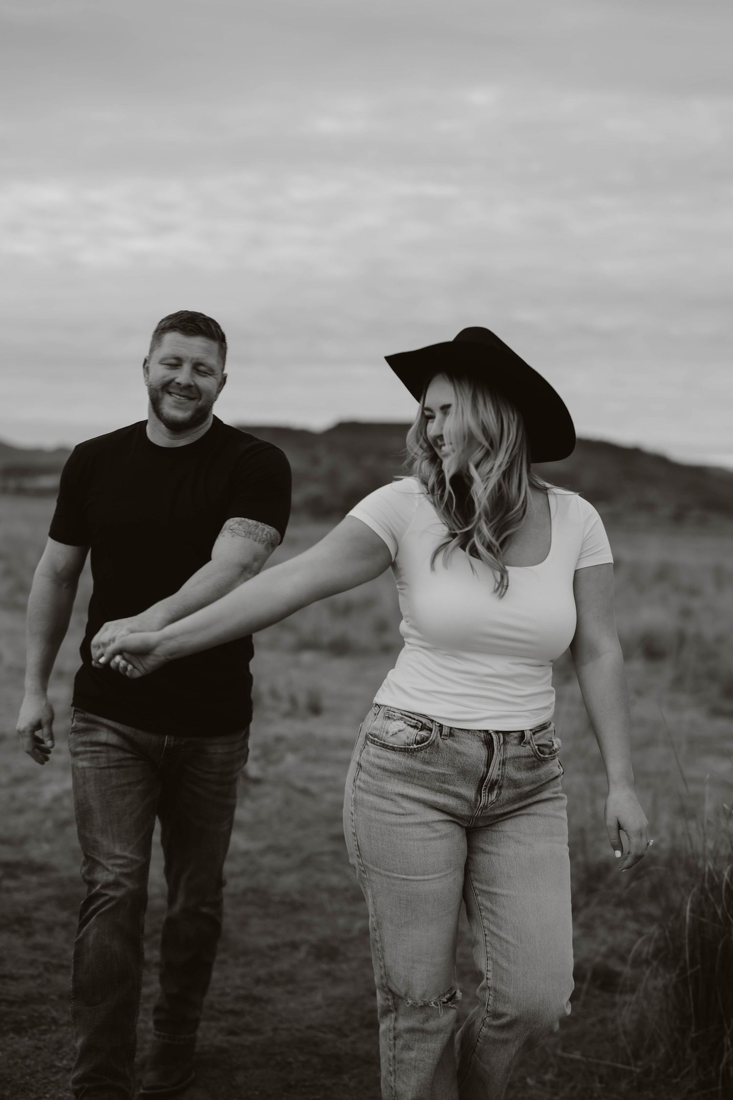 A couple shares candid moments together in a field during a black and white photoshoot.