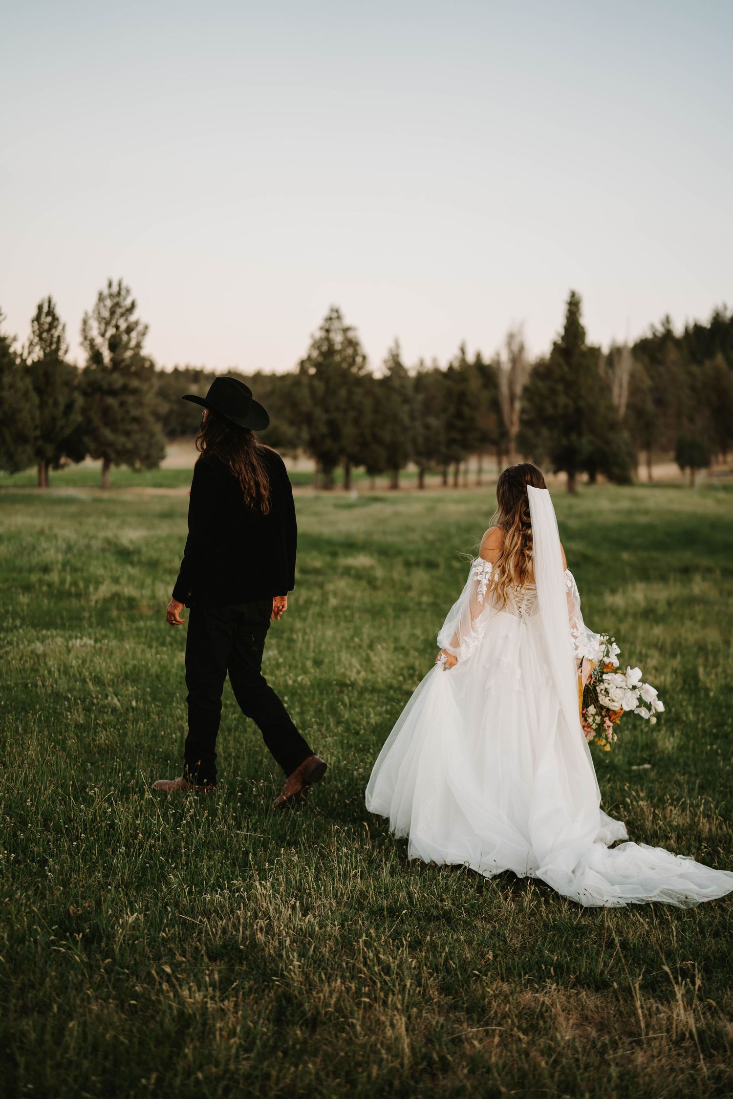 Wedding couple walking through a green meadow at dusk.