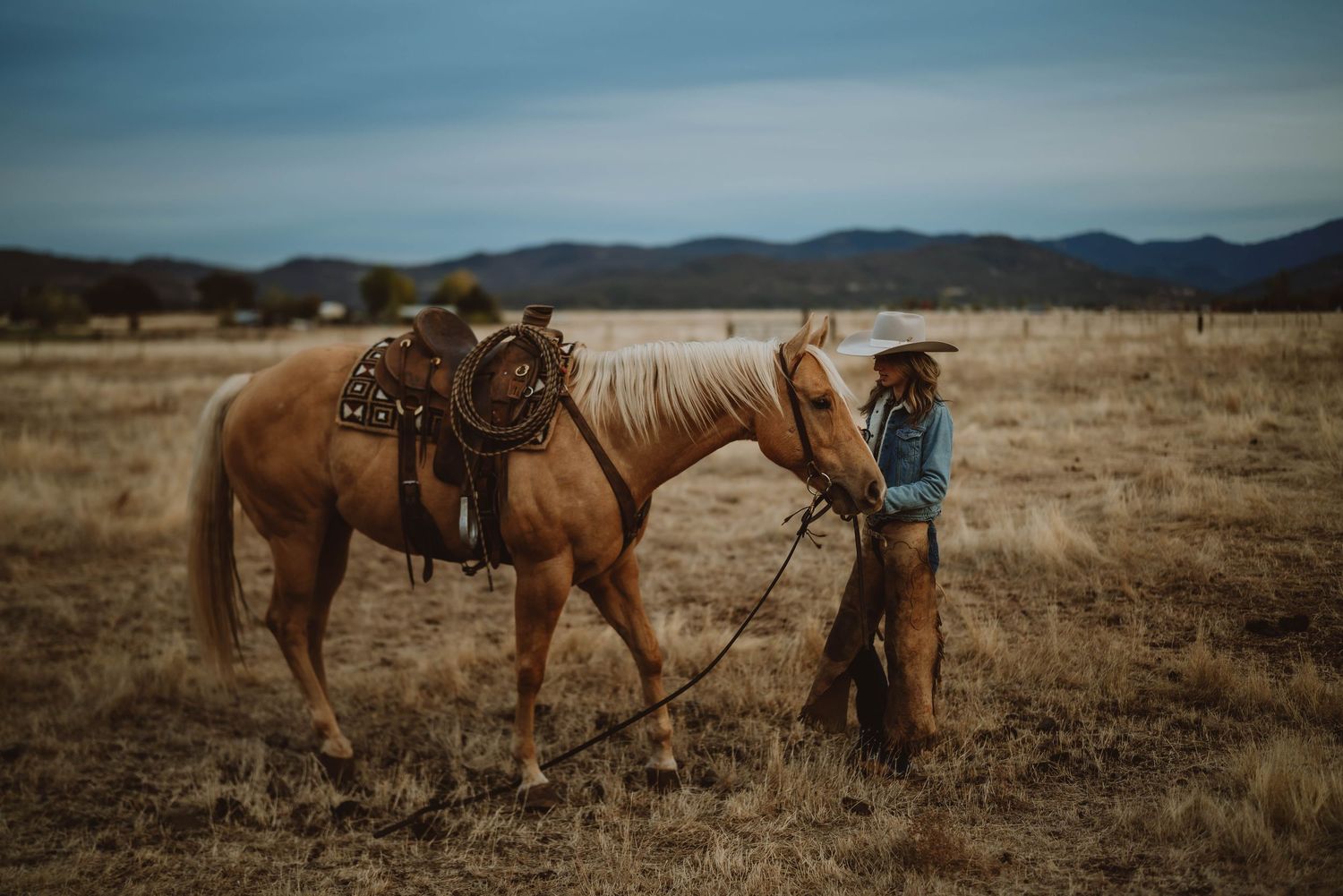 Horses and riders traverse an expansive desert landscape under cloudy skies.