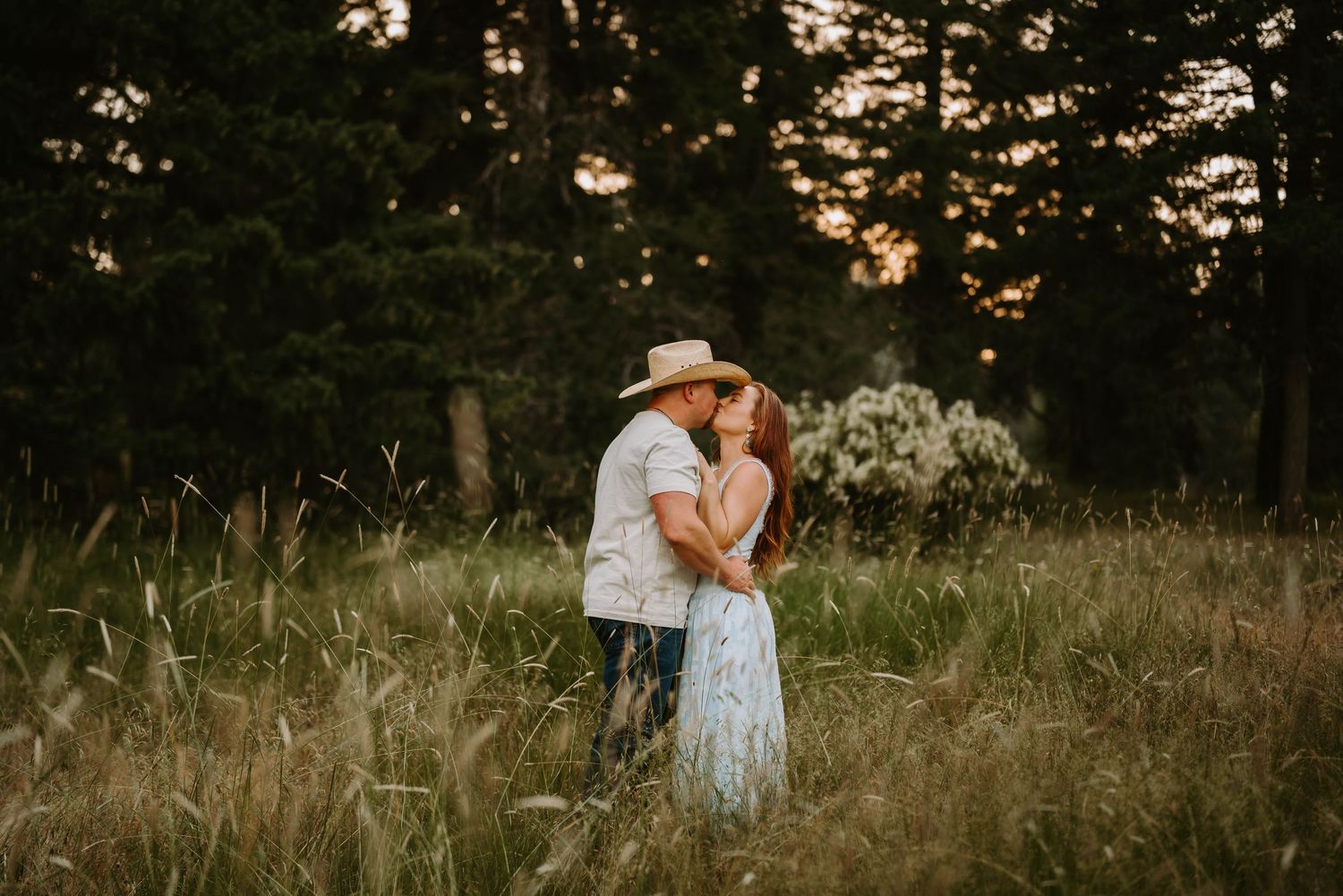 A couple walks through a meadow at sunset holding hands.