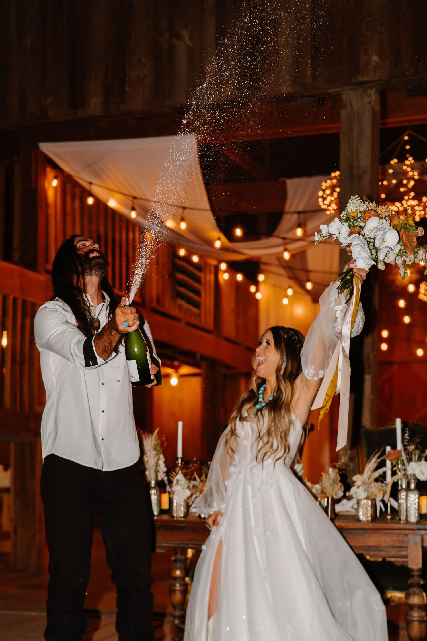 Newlyweds share their first dance in a rustic barn venue decorated with twinkling lights.