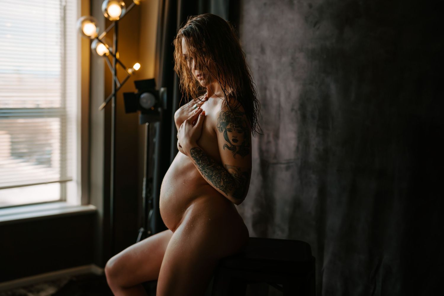 Moody boudoir photography session with window light creating dramatic shadows.