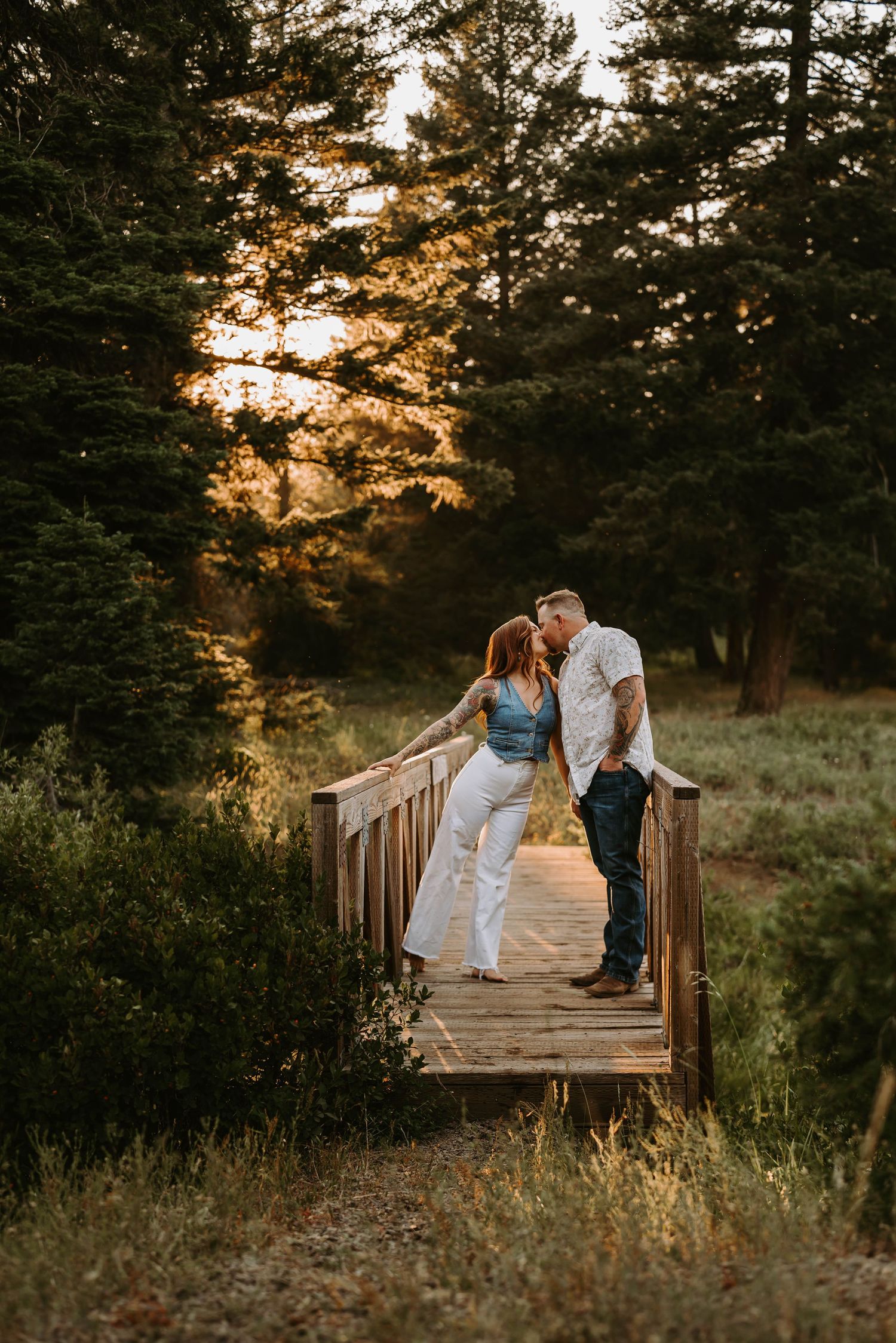Sunset engagement photo on rustic wooden bridge surrounded by pine trees.