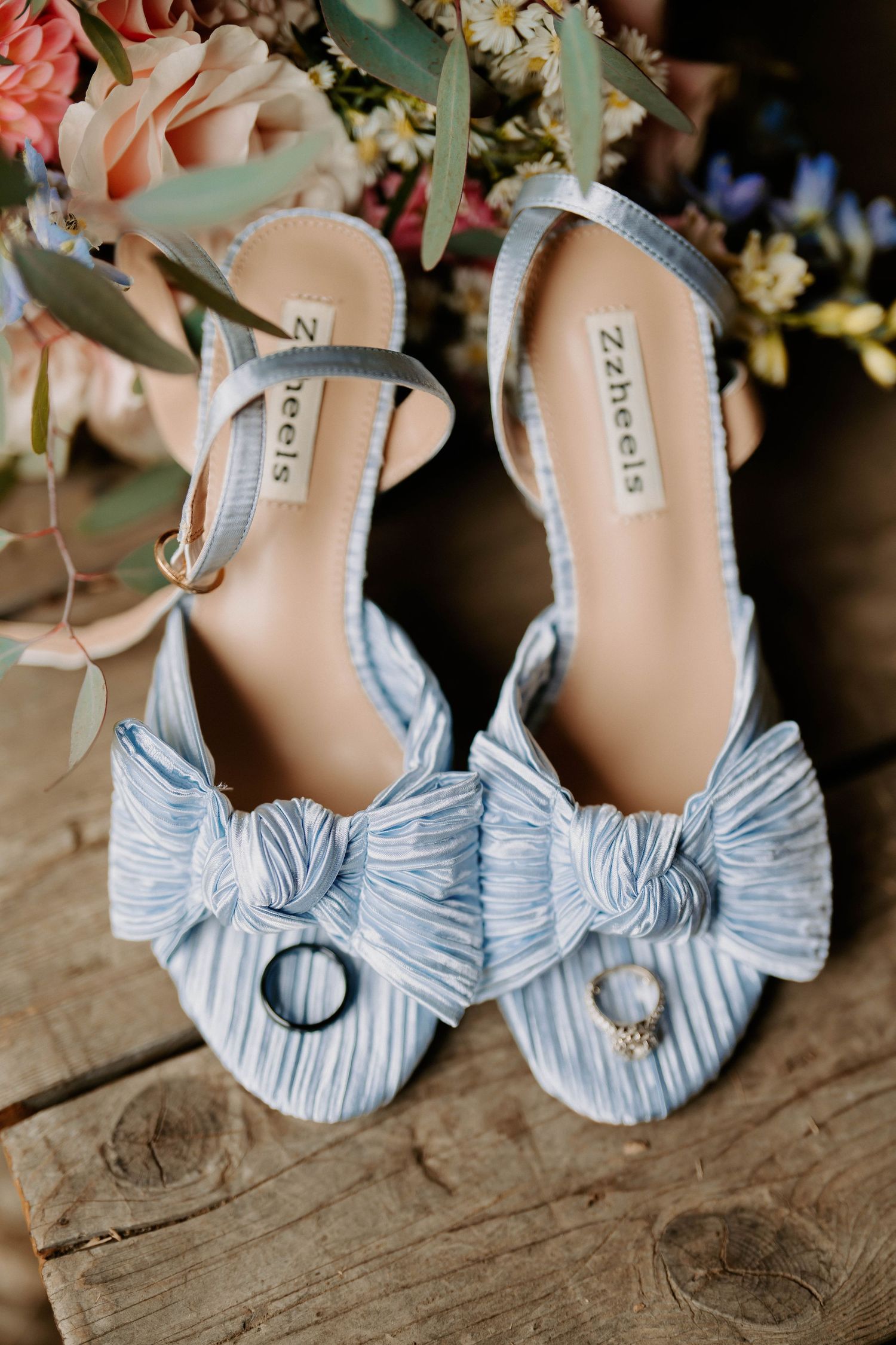 Light blue striped wedding shoes with bow details photographed on wooden surface.