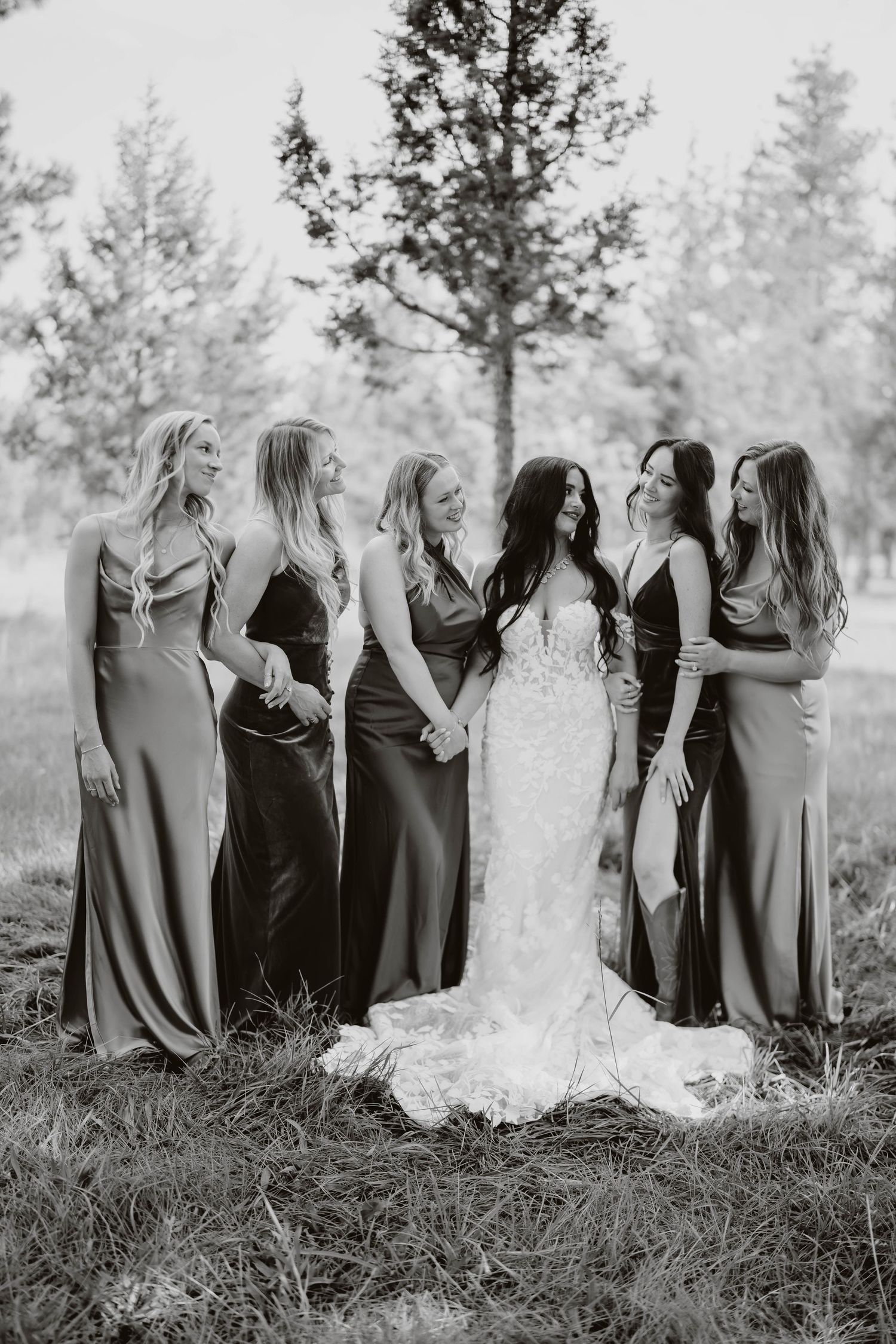 Black and white photo of a bridal party in long dresses standing together outdoors.