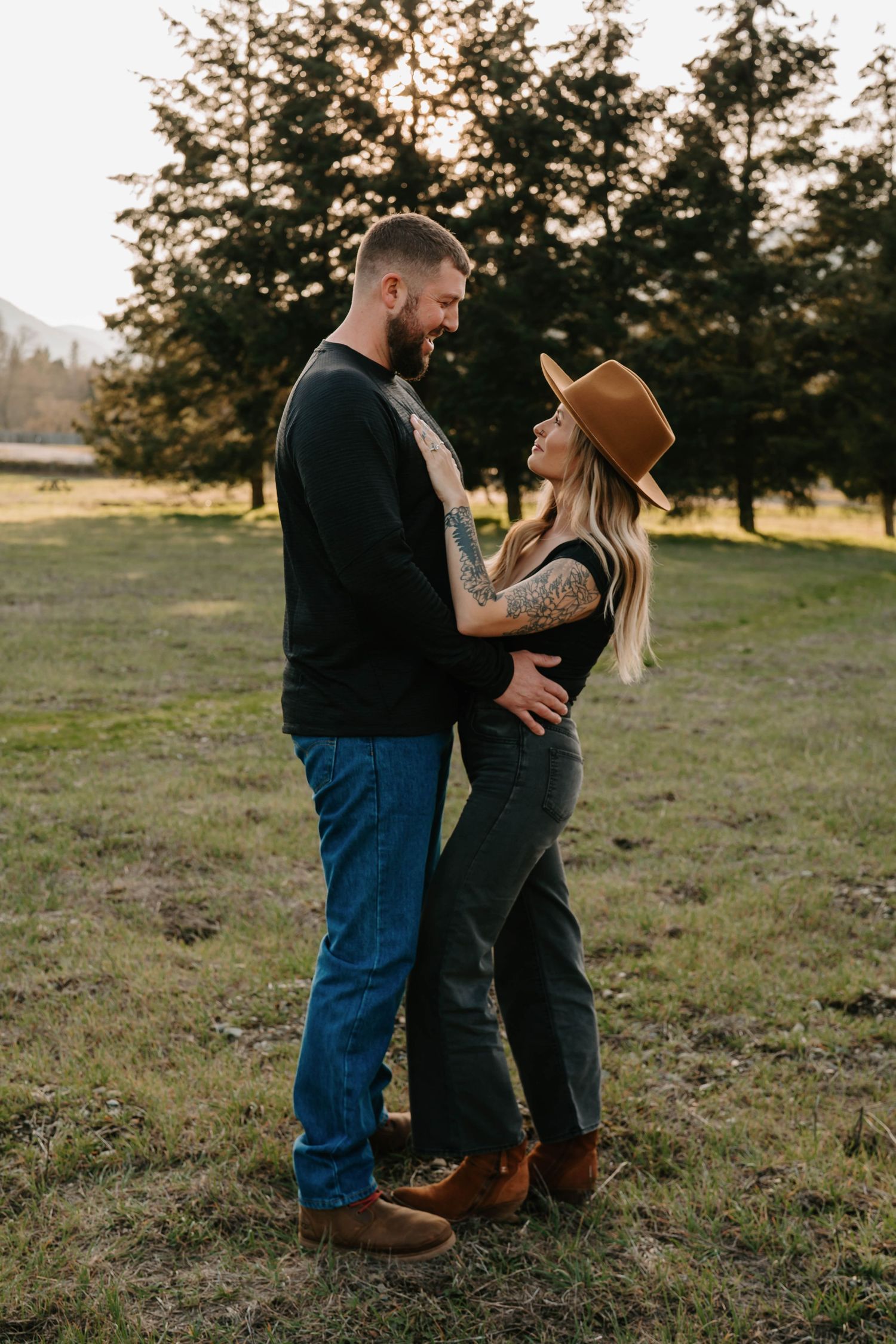 Couple sharing intimate moment in field during sunset with trees in background.