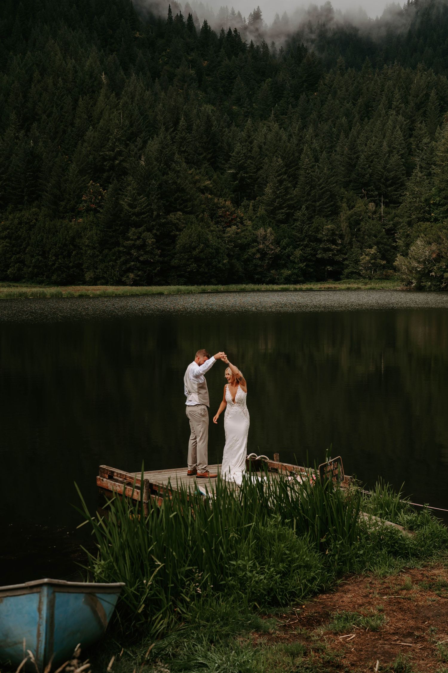 A couple shares an intimate moment on a wooden dock overlooking a tranquil mountain lake.