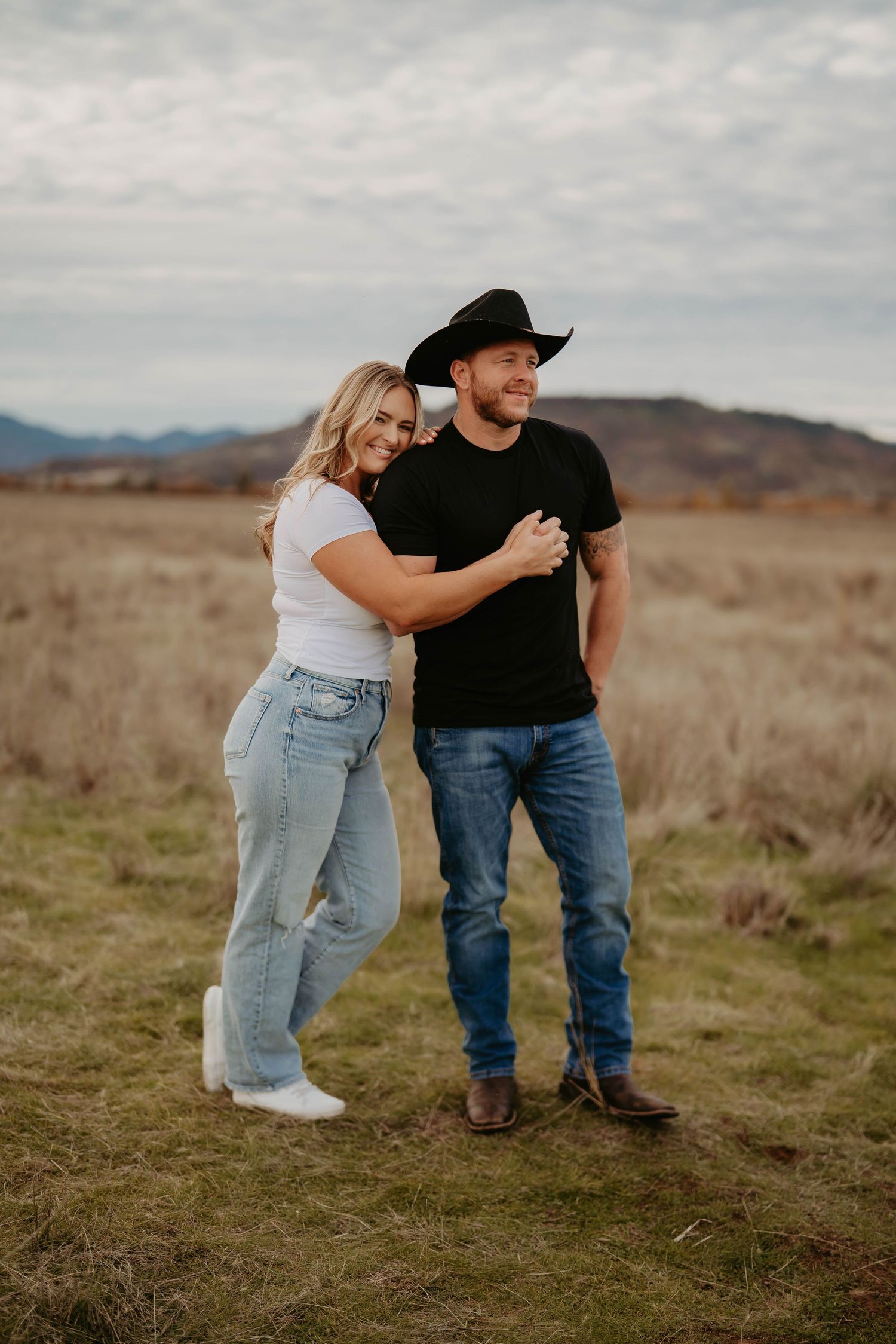 Playful couple interaction on grassy hillside with mountains in background.
