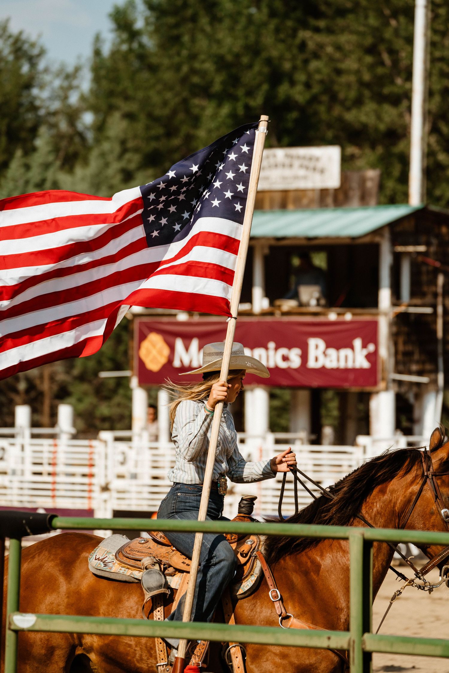 American flags wave above horses at a rodeo arena with Mechanics Bank sign visible.