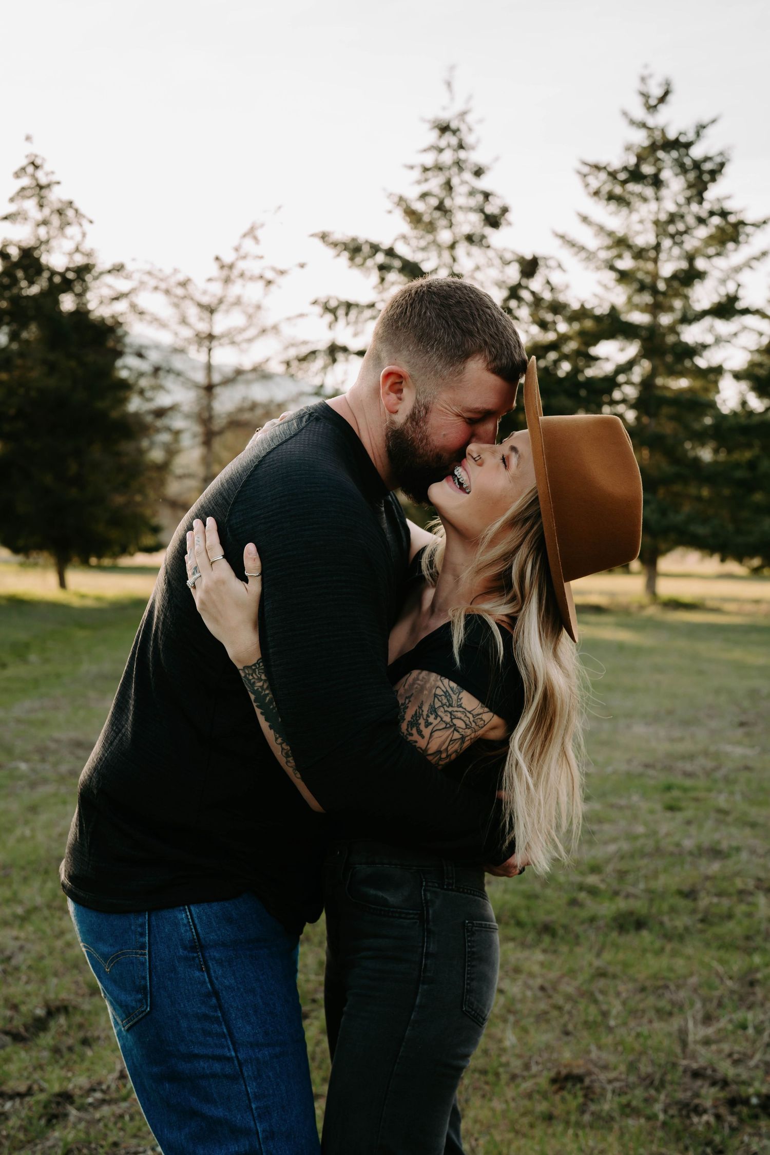 Romantic couple embracing in outdoor setting with evergreen trees.
