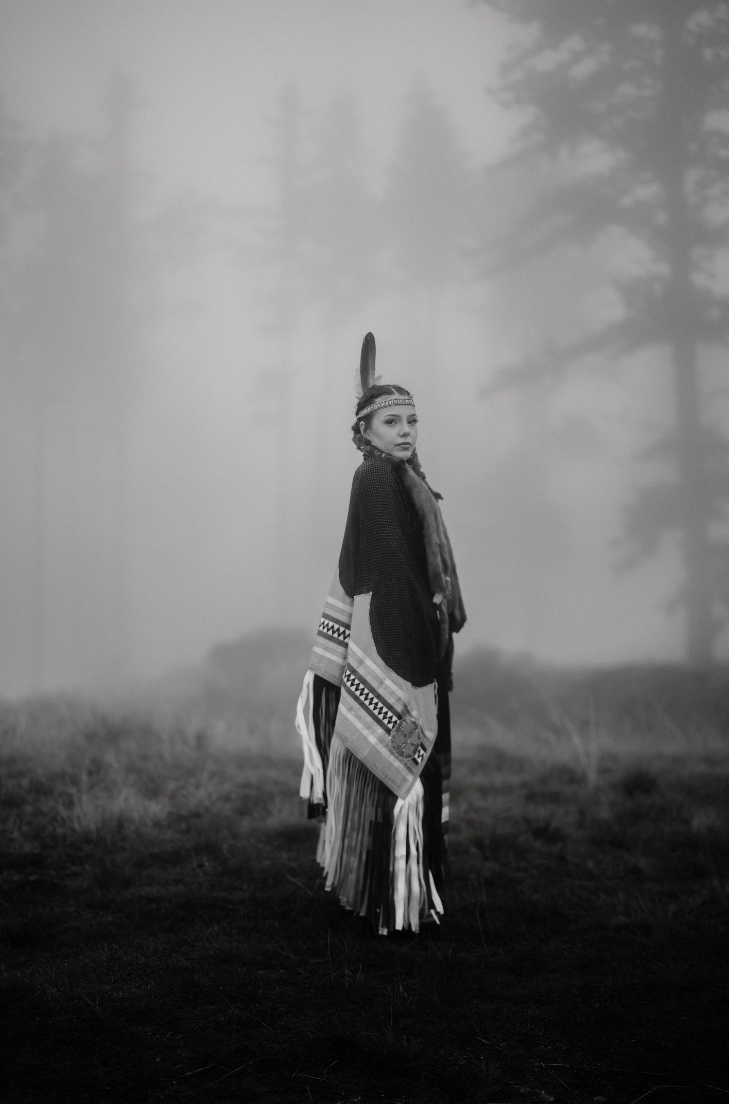 A figure in traditional dress poses with a rifle against foggy wilderness backdrop.
