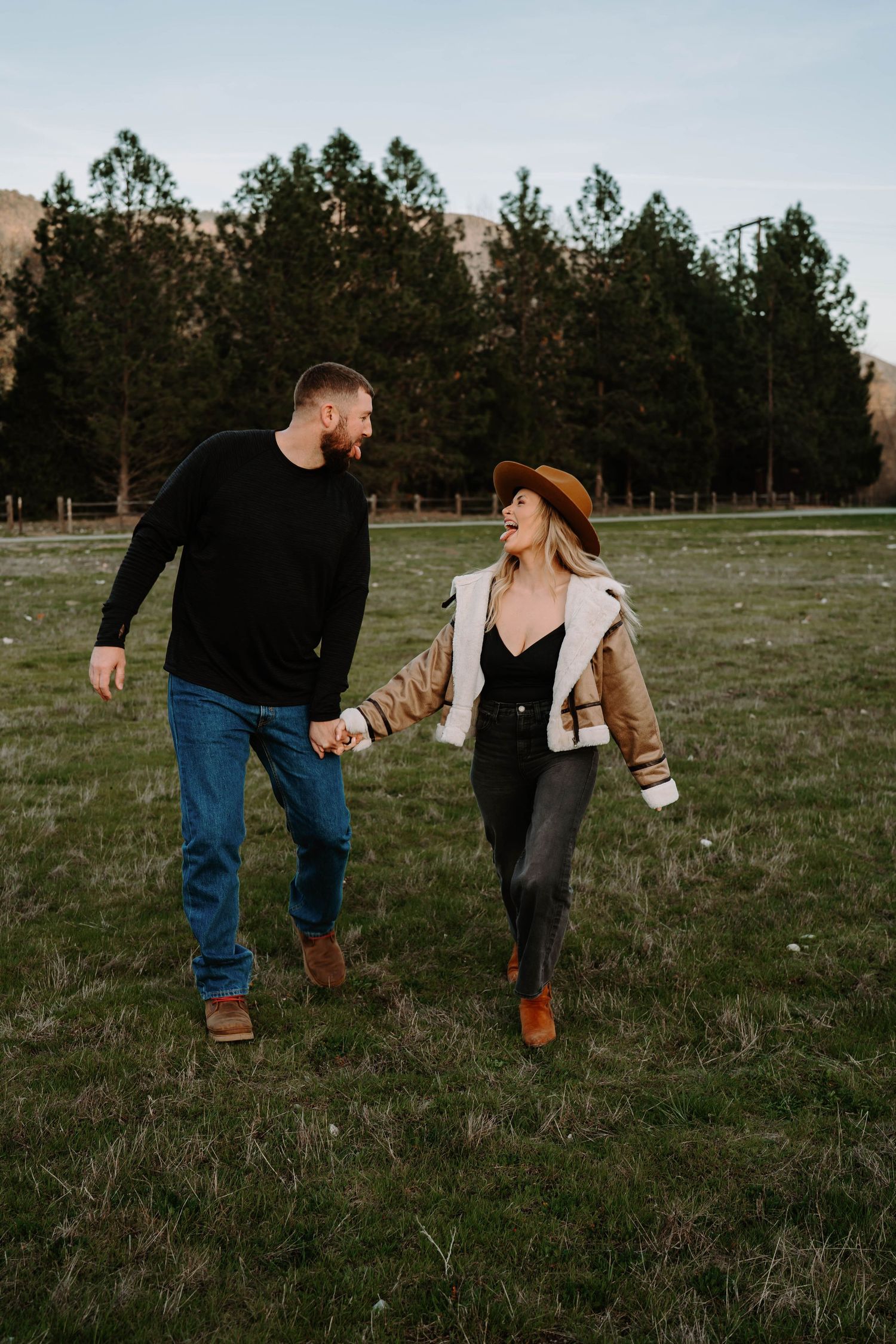 Playful couple running and laughing together in an open field at dusk.