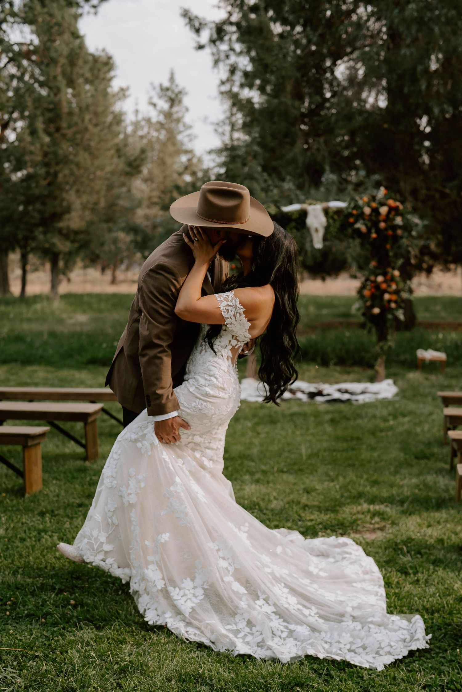 Elegant lace wedding dress with a flowing train photographed in a rustic outdoor setting.
