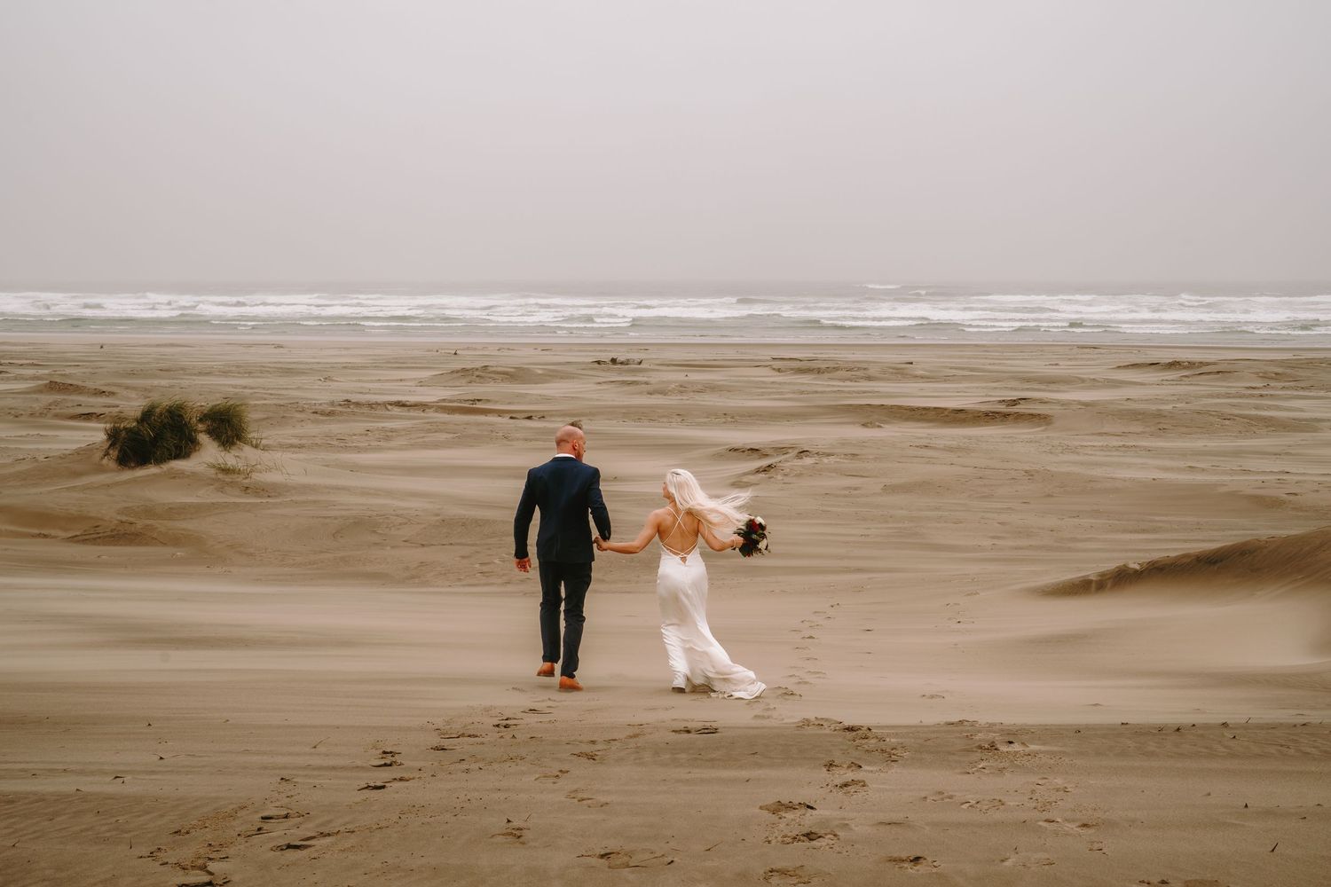 A distant view of a couple walking along a misty beach shoreline.