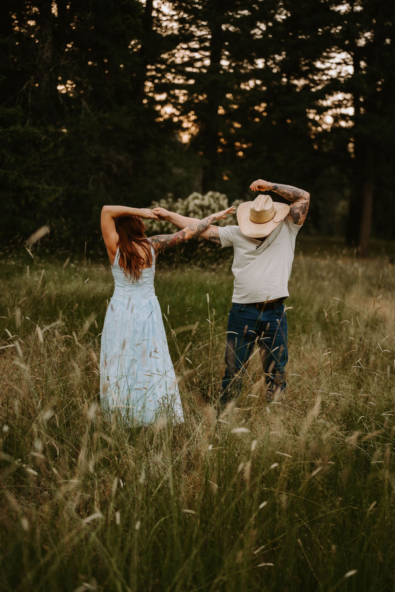 A couple dances through tall grass in a field at golden hour.