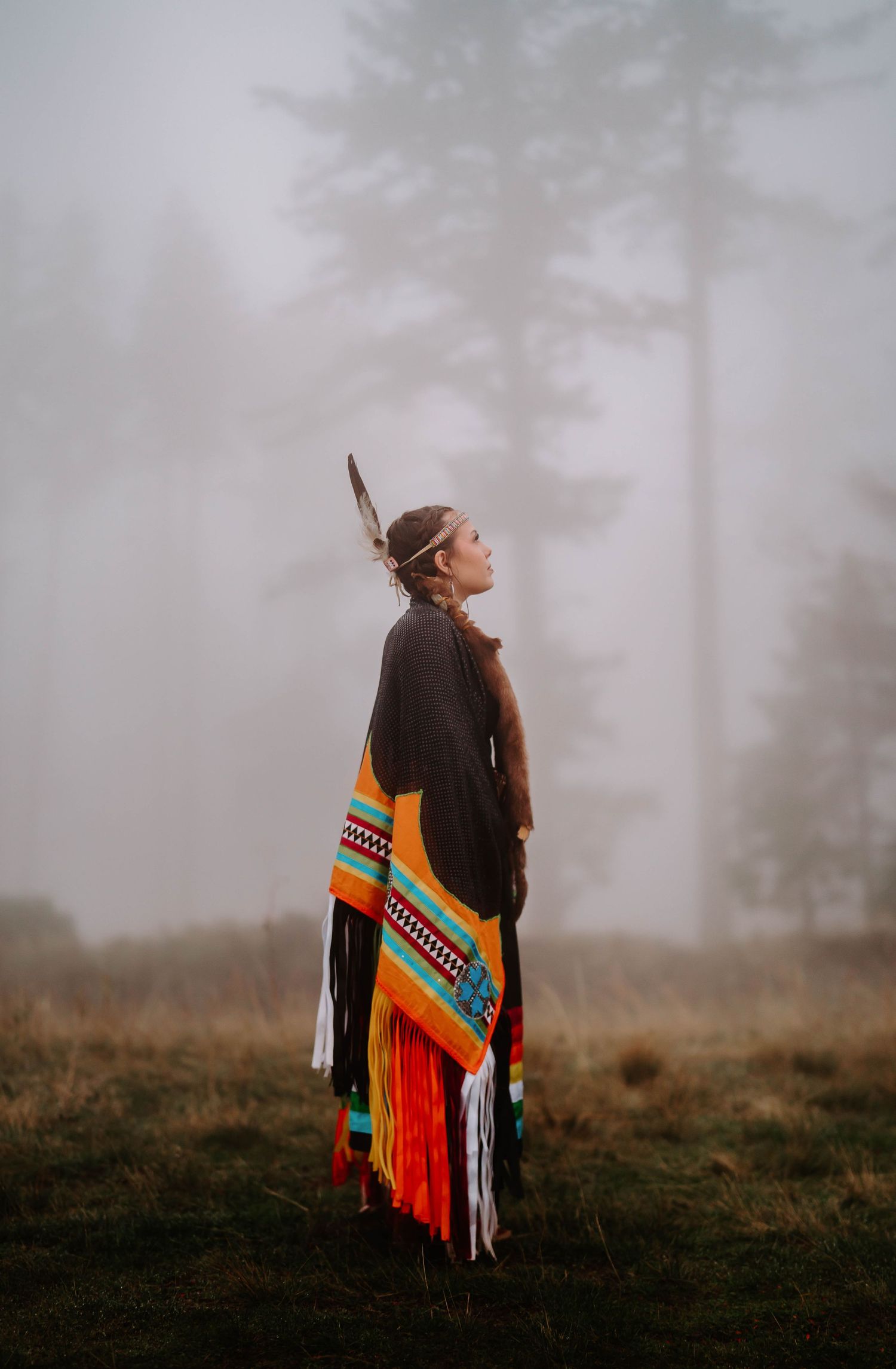 A person in traditional Native American regalia stands in misty forest scenery.