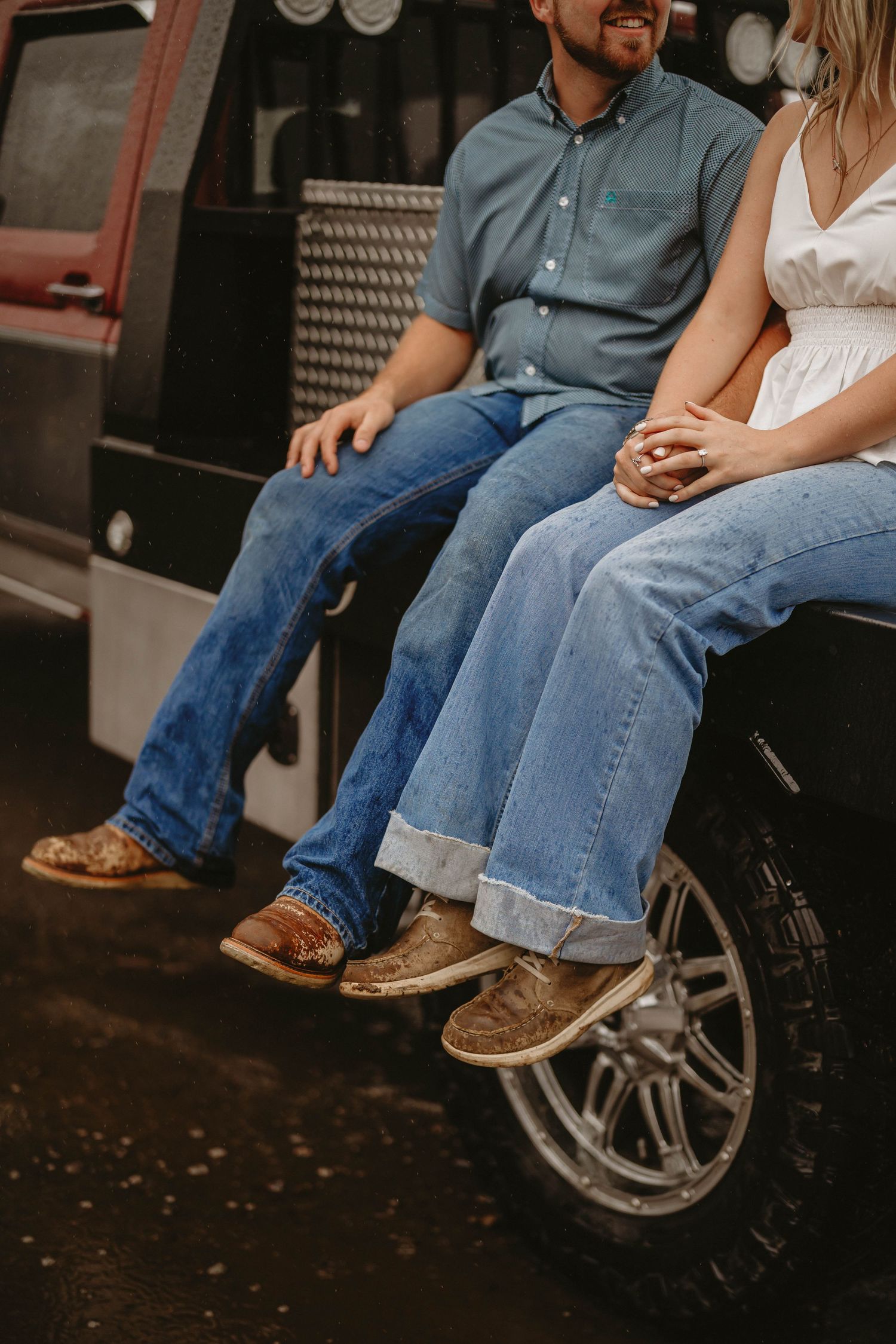 Couple's legs dangling from the back of a rustic truck showing worn boots and jeans.