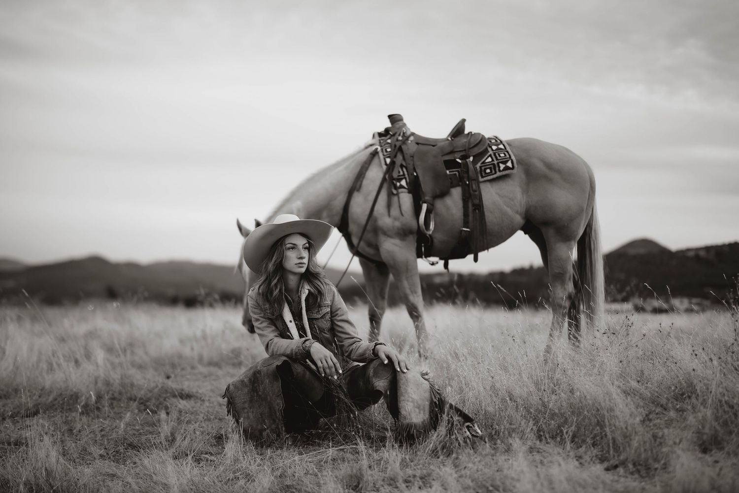 Black and white panoramic view of horses and riders in a rural landscape.