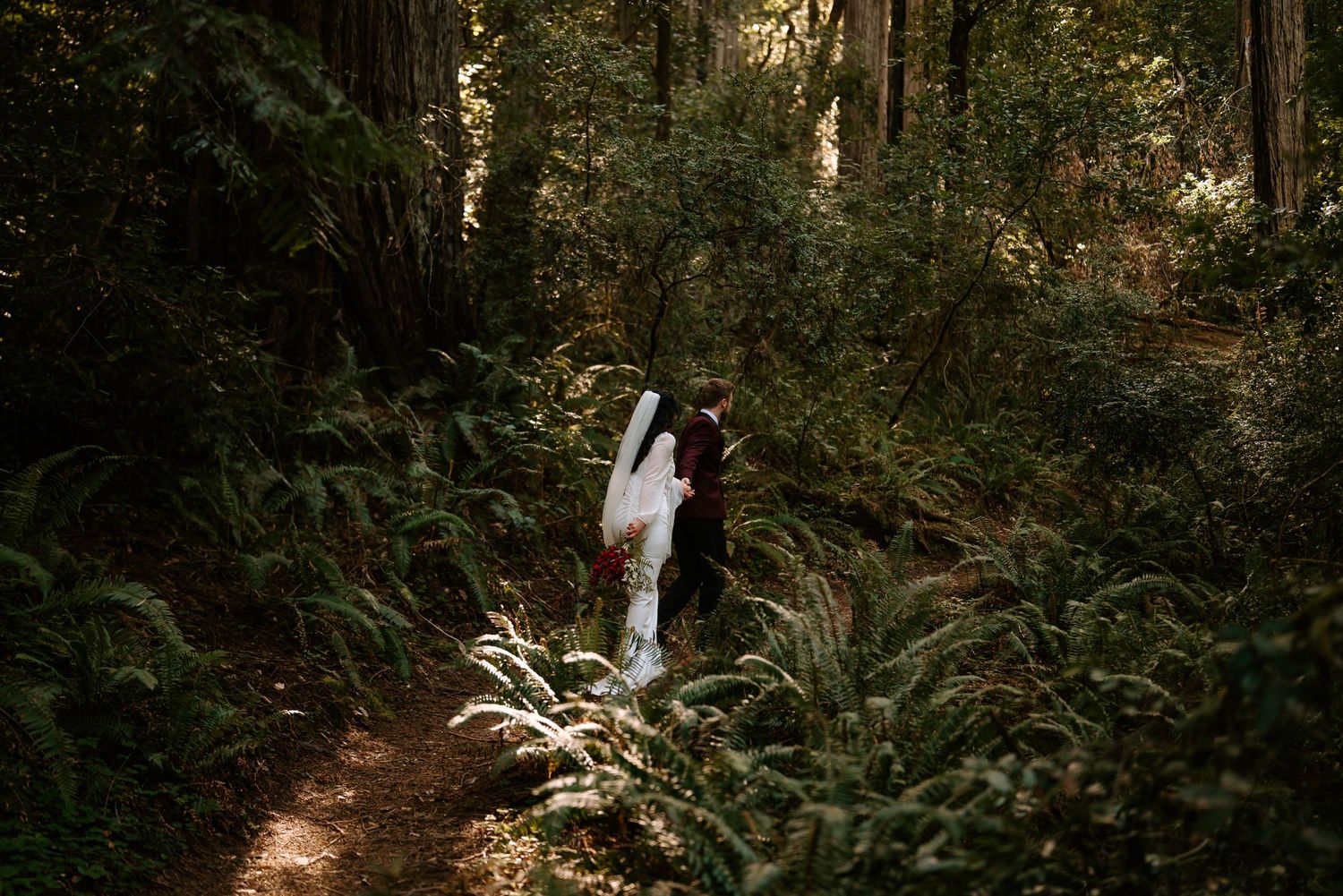 A romantic wedding photo shoot in a sunlit forest with rays of light filtering through the trees.