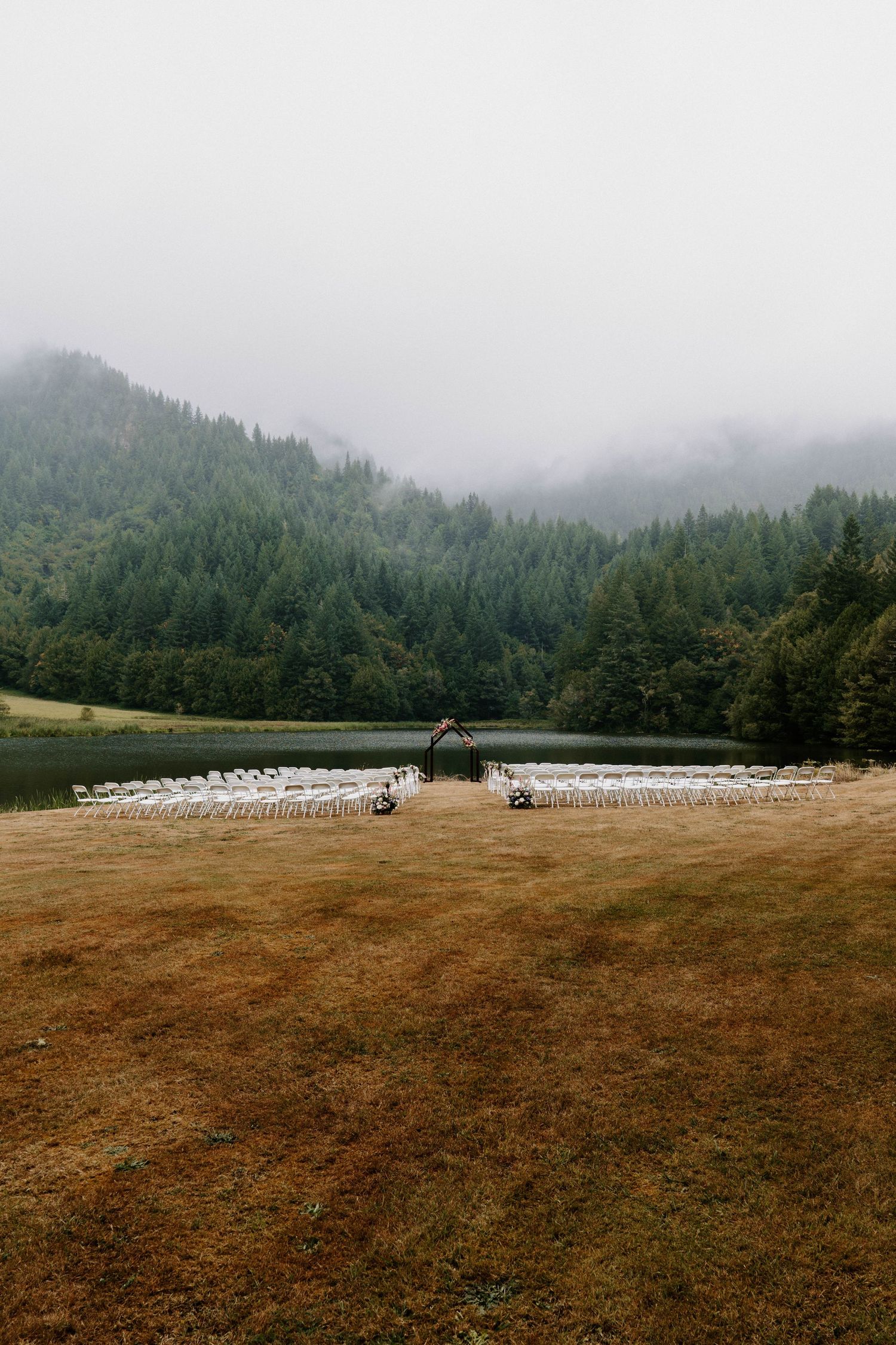 Outdoor wedding venue setup in a mountain meadow with rows of white chairs.