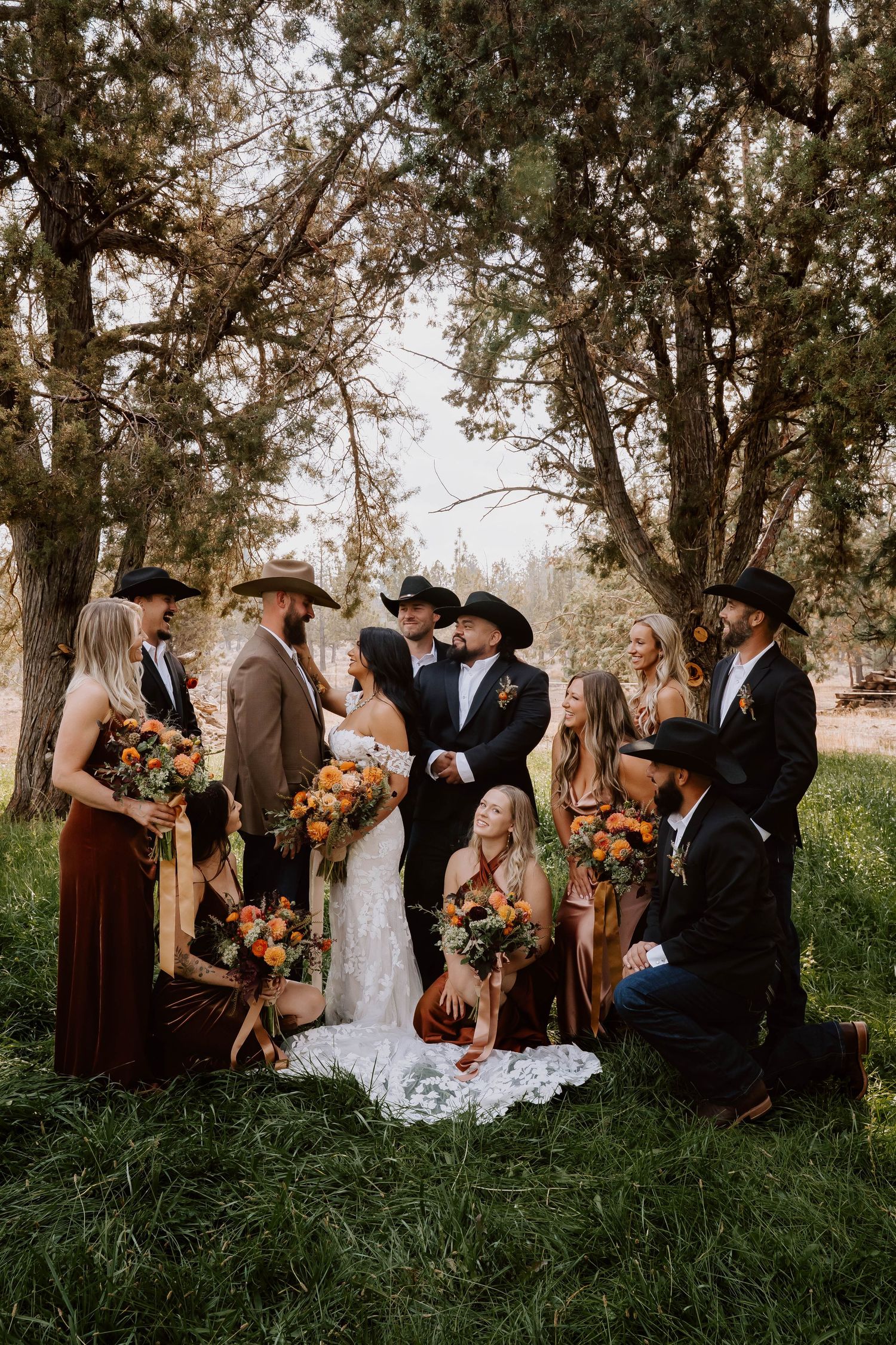 Wedding party in rustic attire celebrates together on grassy hillside during outdoor ceremony.