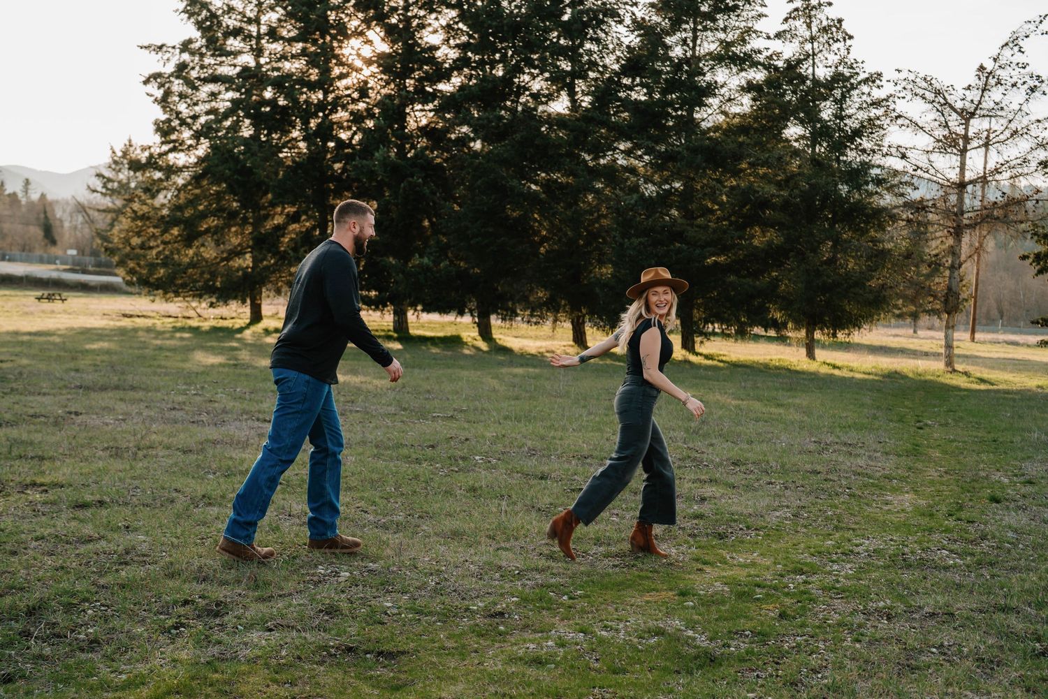 A couple playfully runs and chases each other in a grassy field at sunset.