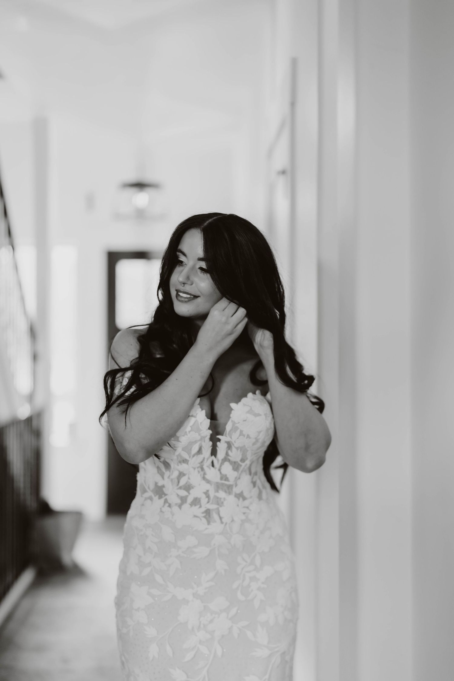 A bride in a delicate white lace wedding dress preparing for her special day in a bright hallway.