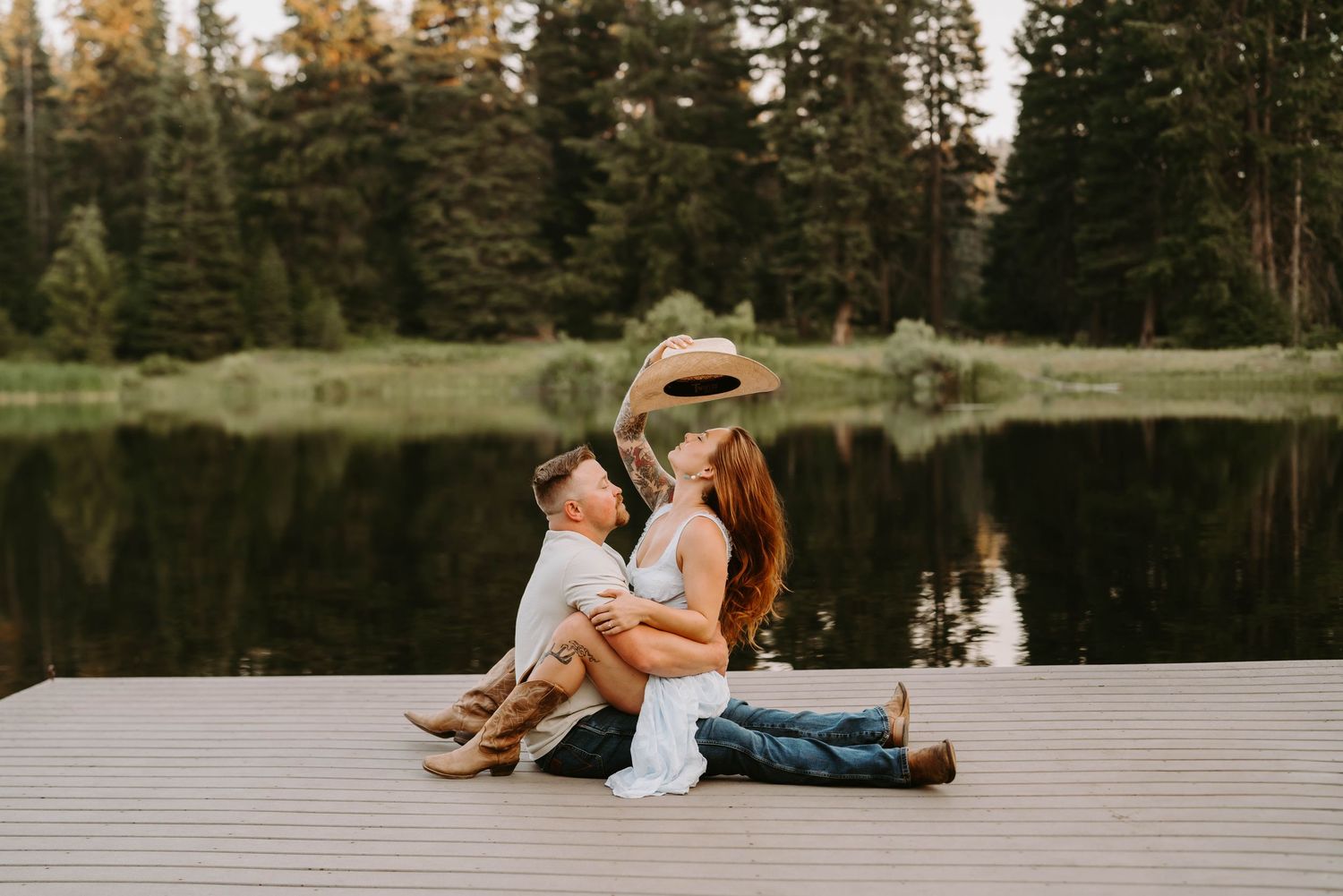 Couple sitting together on dock by peaceful lake surrounded by pine trees.
