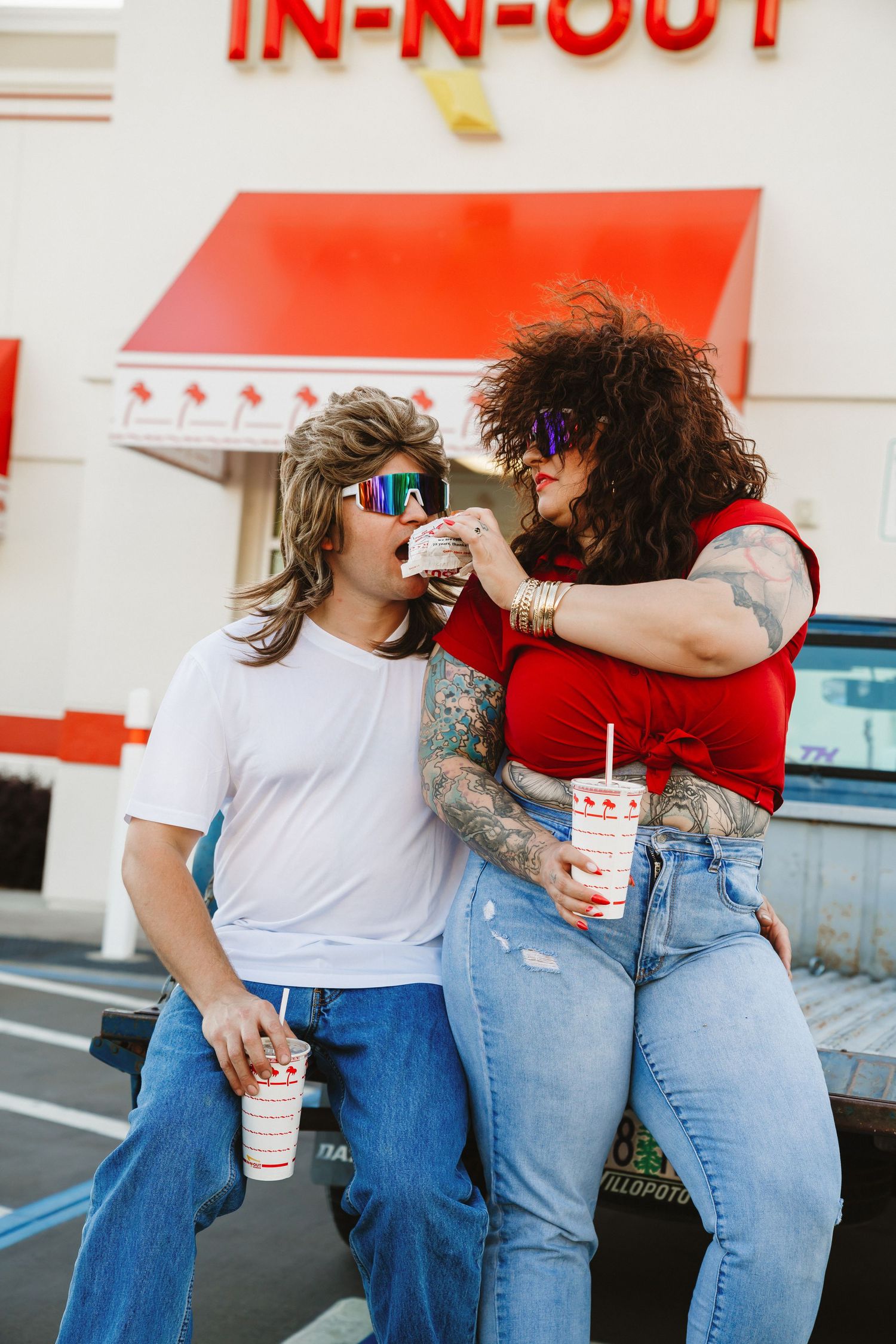 Fun retro-styled couple sharing milkshakes outside In-N-Out burger.