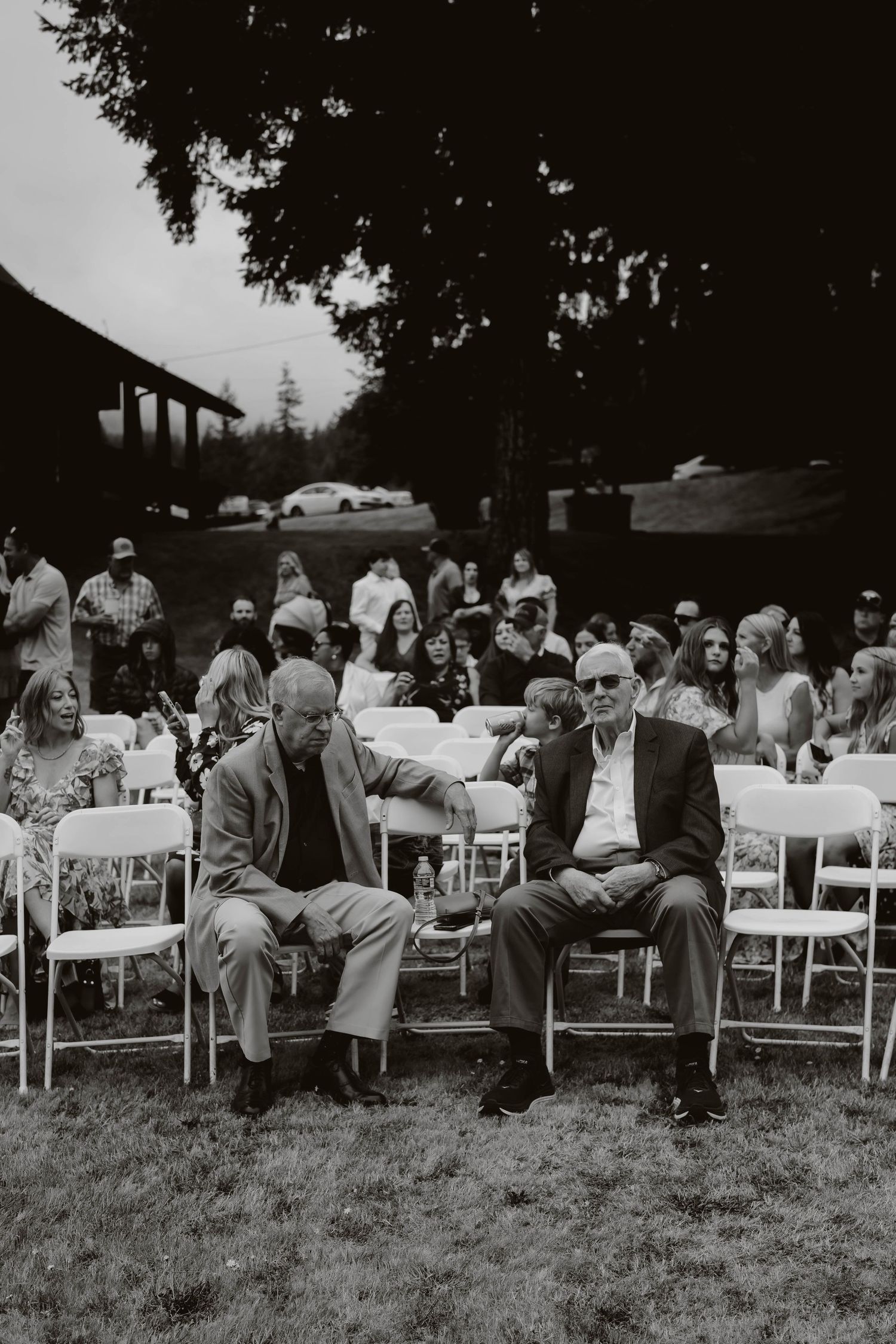 Black and white photo of wedding guests seated in rows of white chairs outdoors.