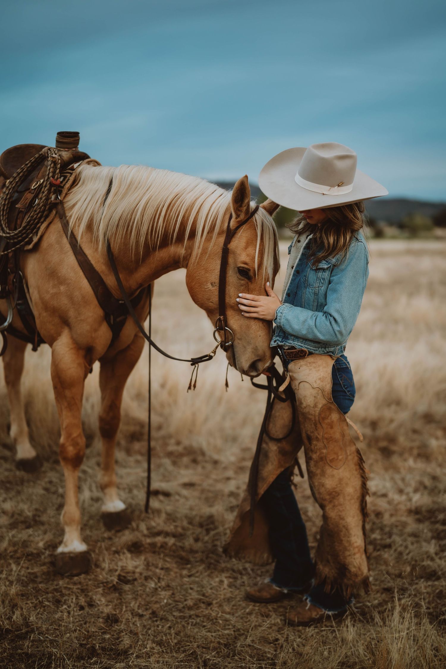 Cowboy boots and chaps shown in detail against a rustic outdoor backdrop with a horse.
