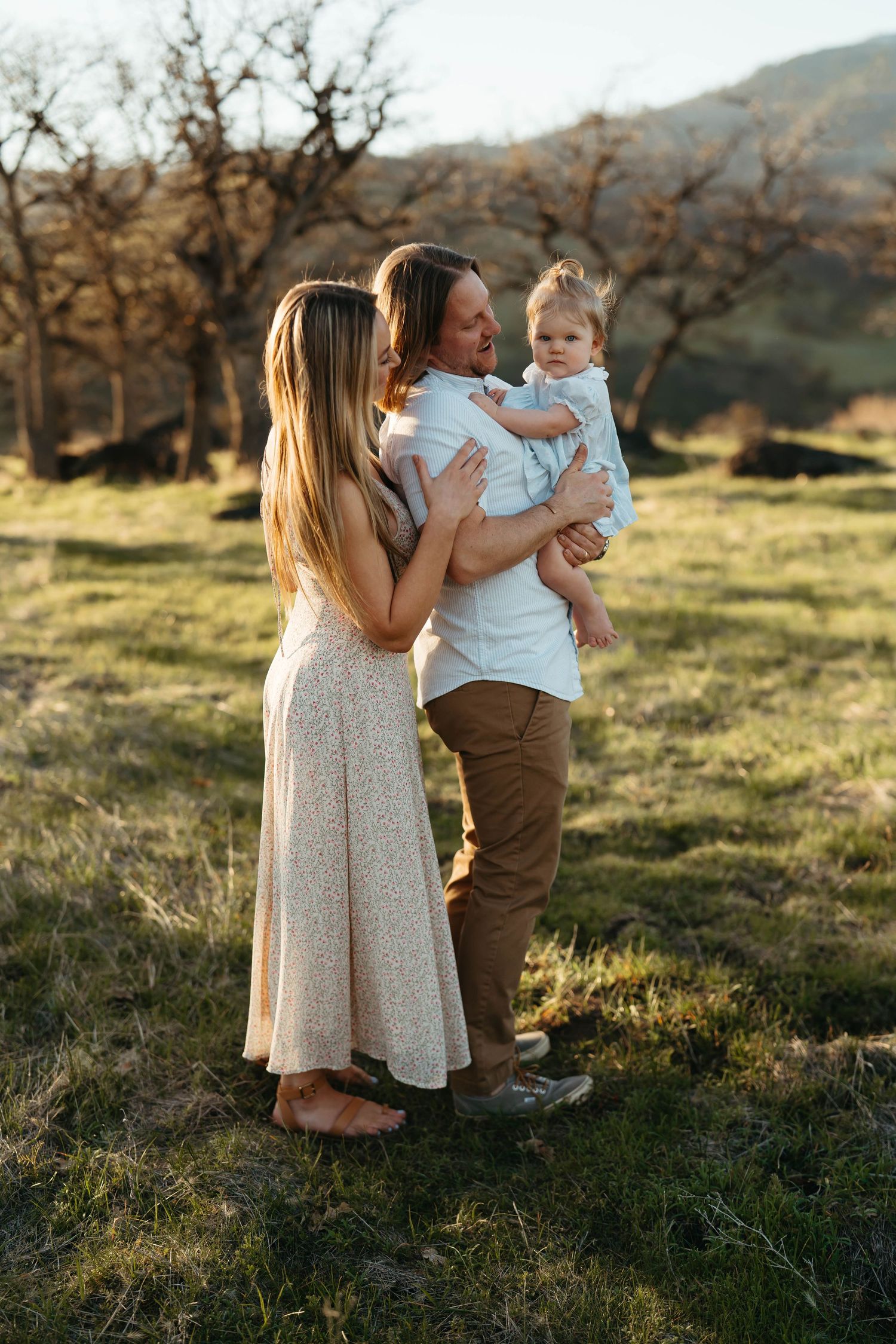 Family moment captured in golden sunlight on grassy hillside.