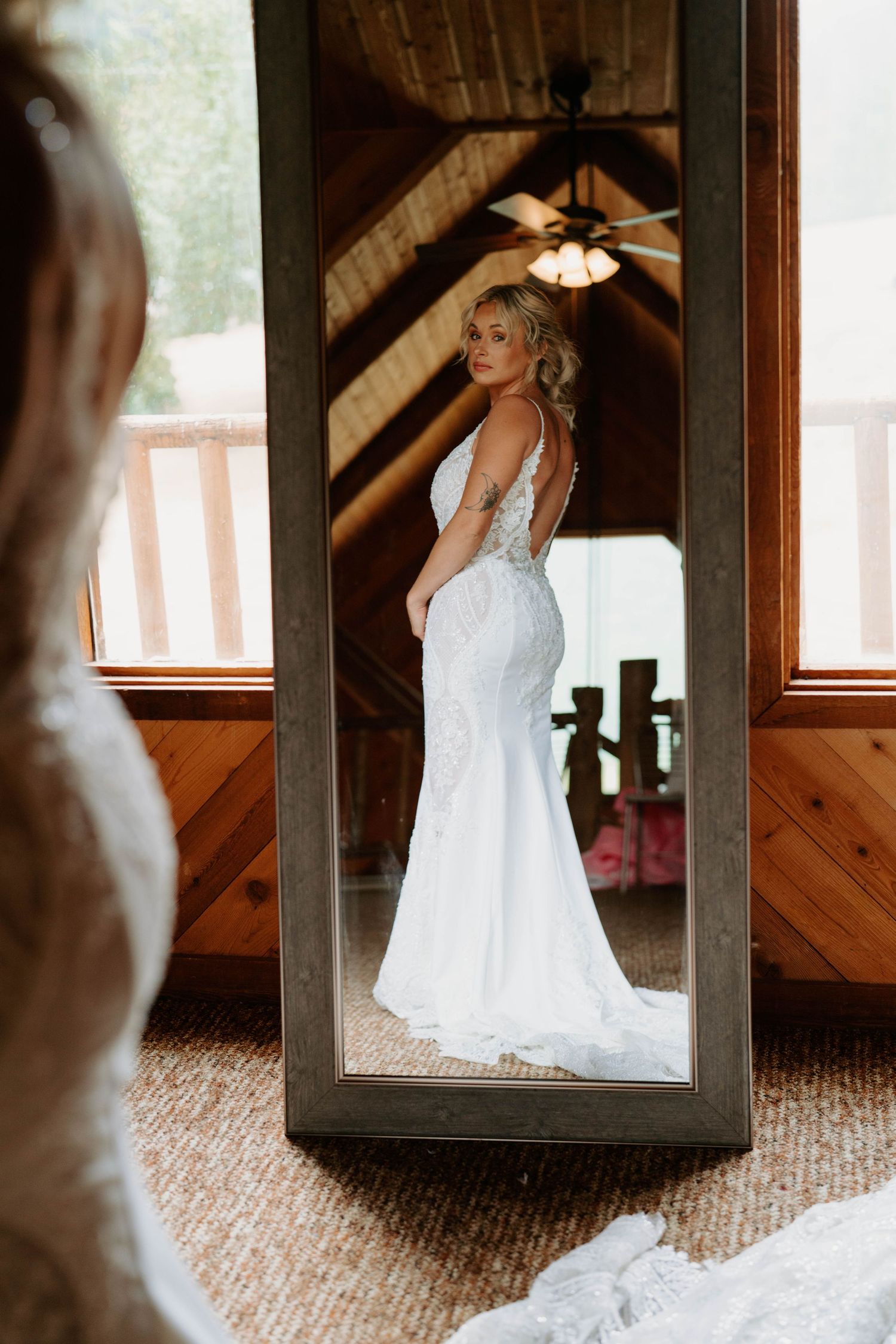 Wedding dress photographed through wooden mirror frames in rustic indoor setting.