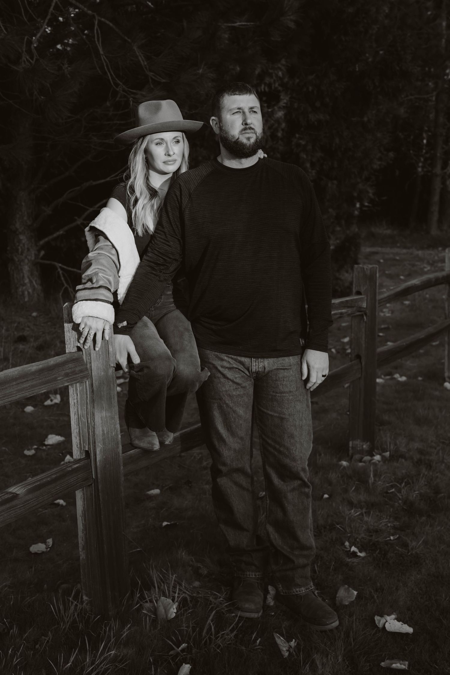 A couple poses together in black and white on a rustic wooden fence.