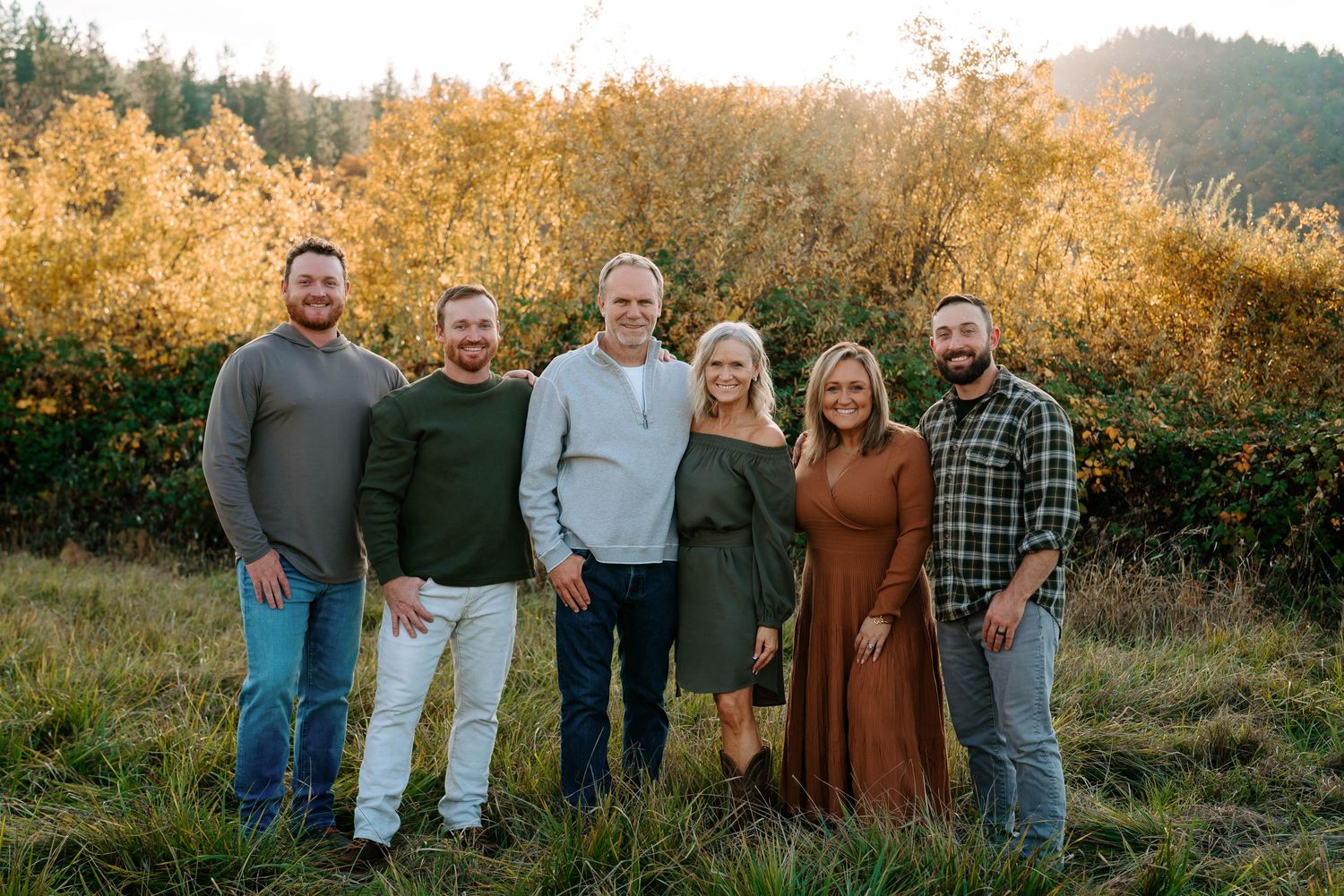 Group photo of people standing together in golden sunset light on grassy hillside.