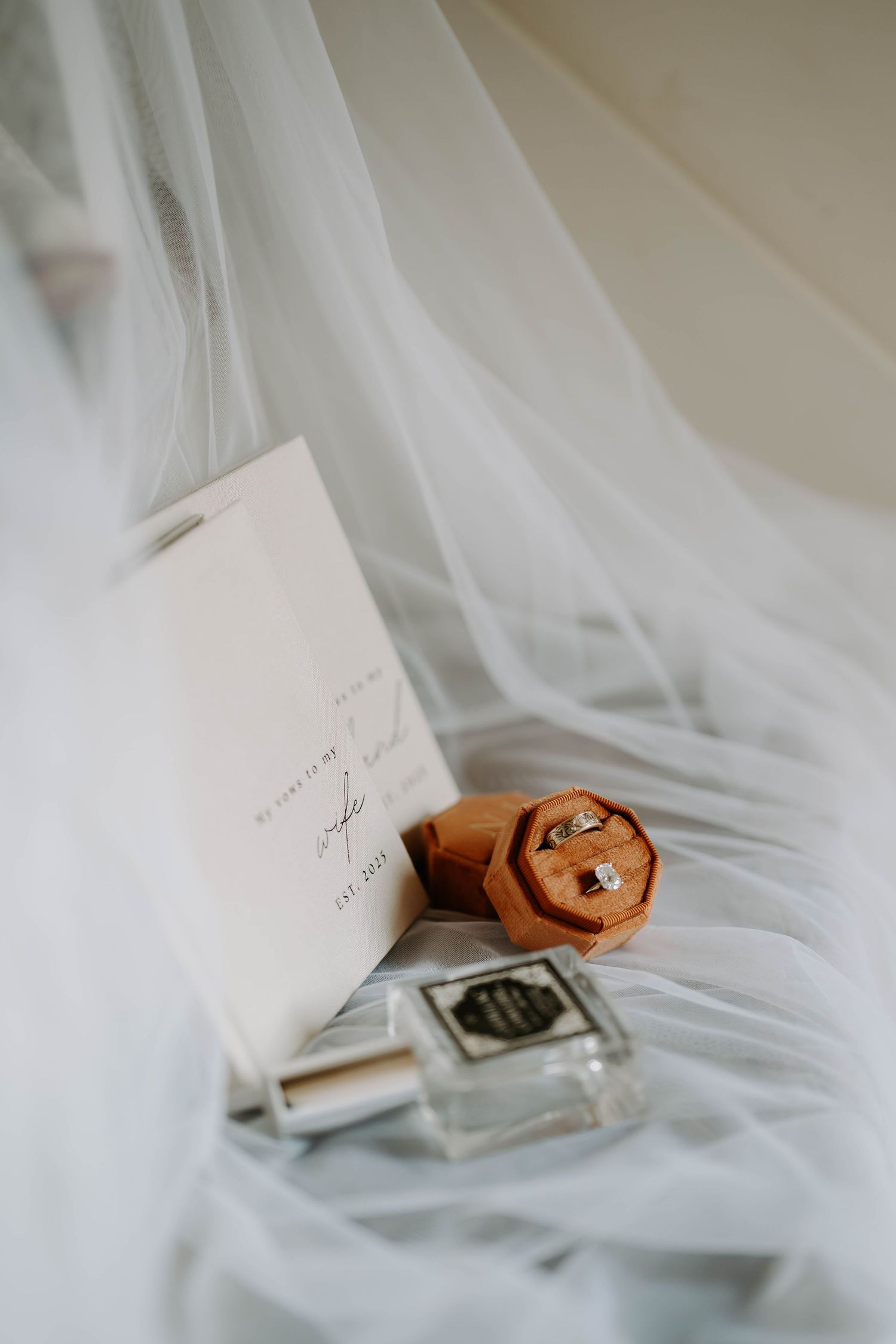 Delicate white veil draping over wedding stationery and details.