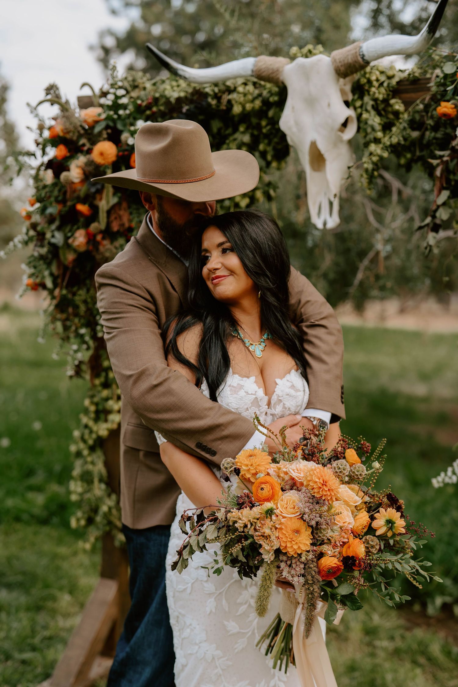 A romantic wedding photo in an orchard with a beautiful bouquet of orange flowers and dried grasses.