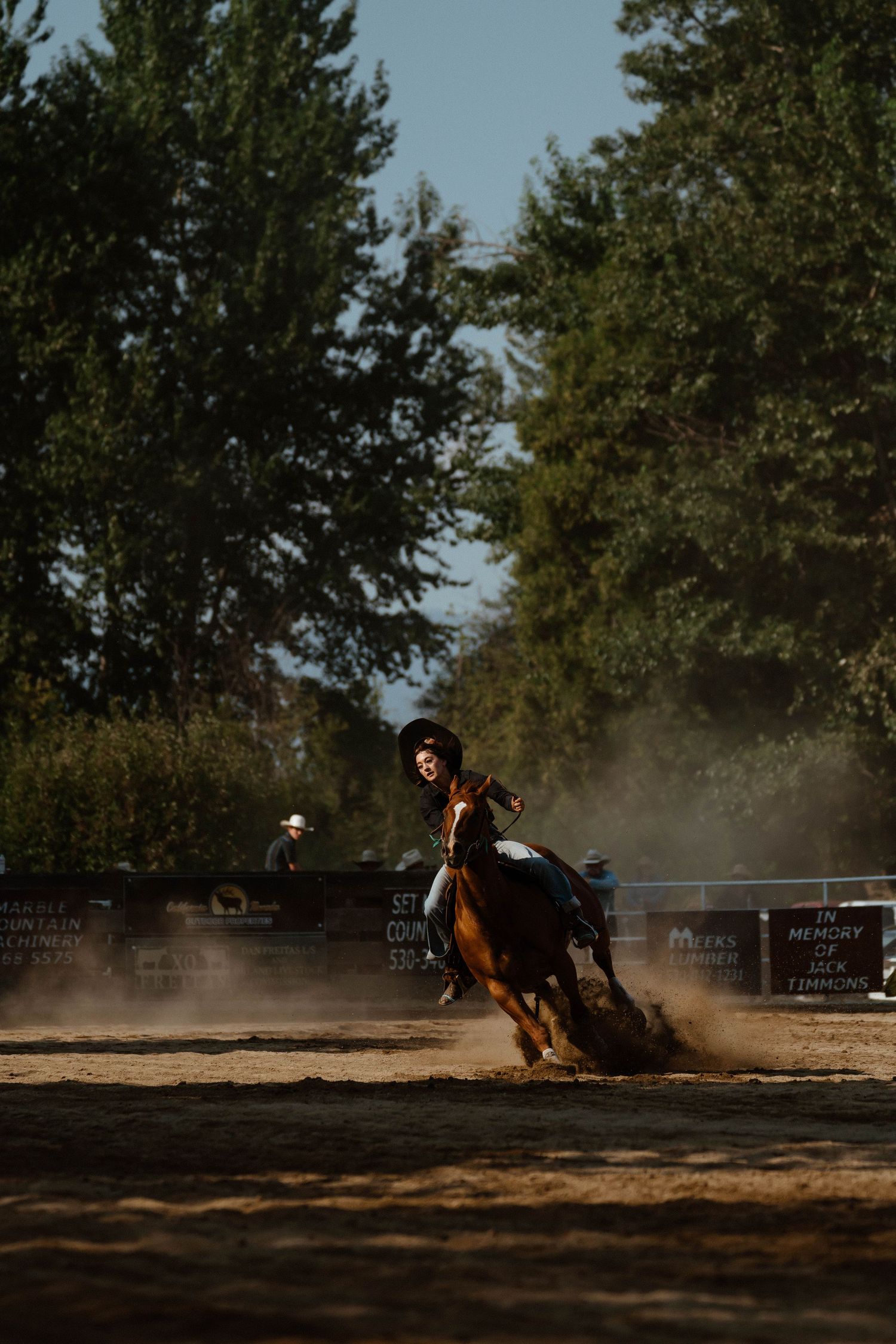 Horse and rider navigate a barrel racing course in dramatic late afternoon light.
