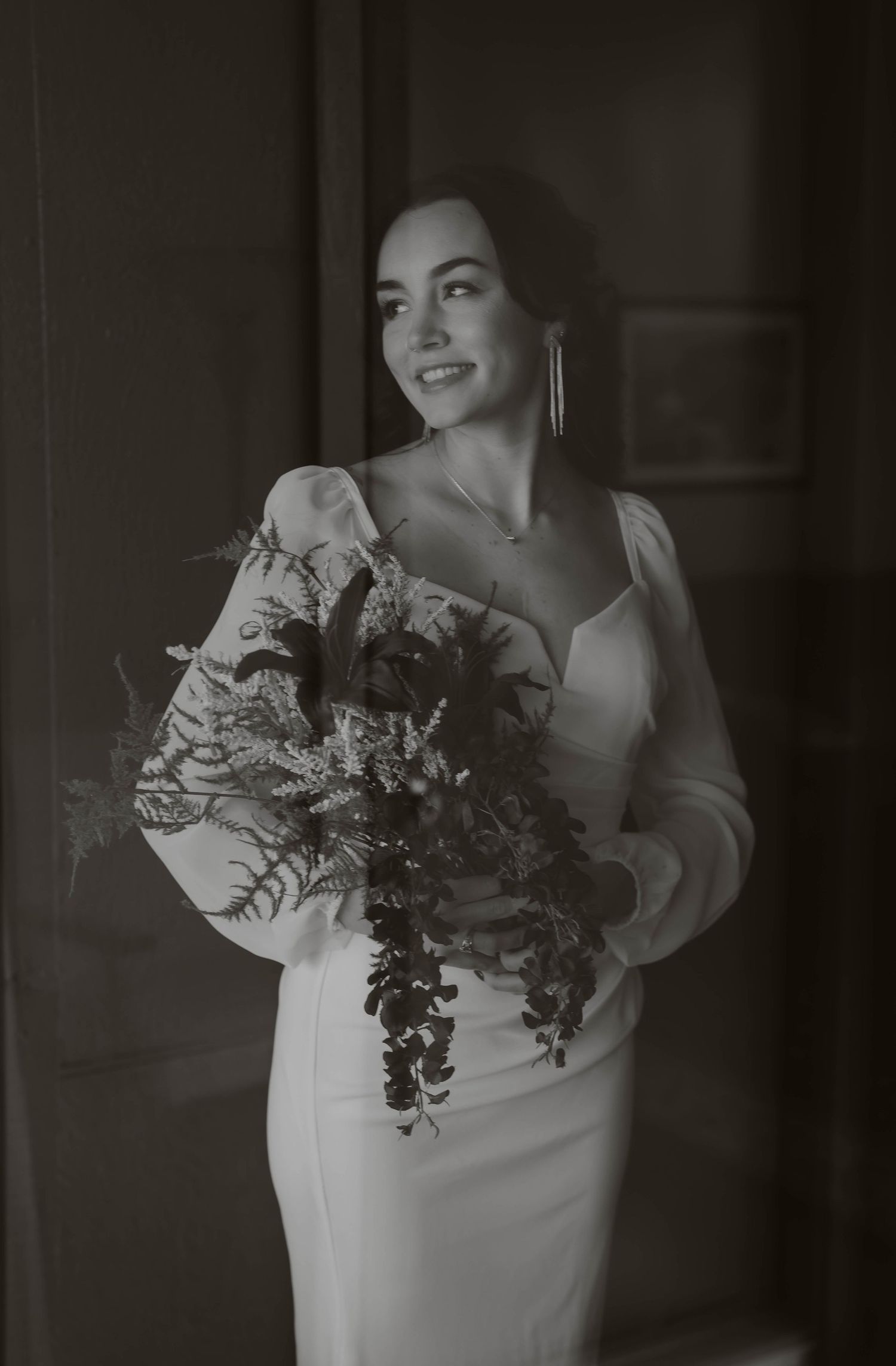 Black and white portrait of a bride holding a cascading bouquet in dramatic lighting.