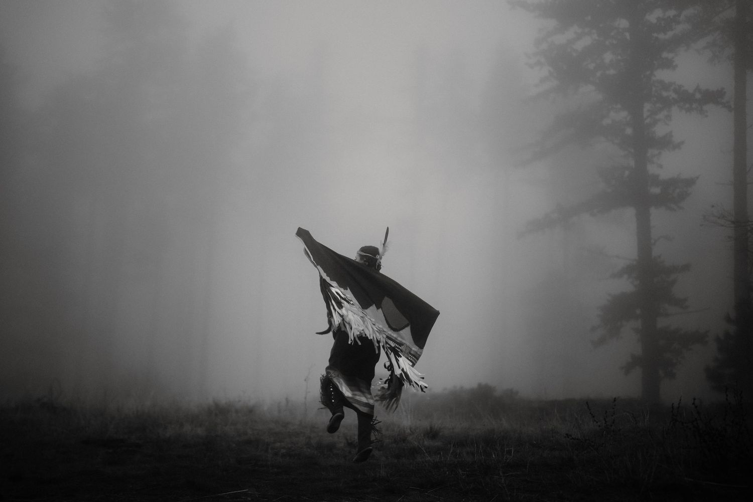 Silhouettes move through atmospheric foggy landscape carrying ceremonial items.