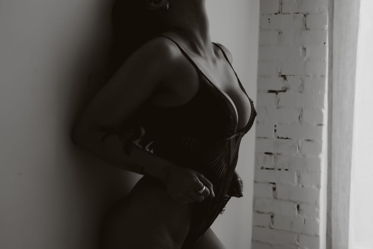 Artistic black and white silhouette of a figure reclining against a white wall in dramatic lighting.