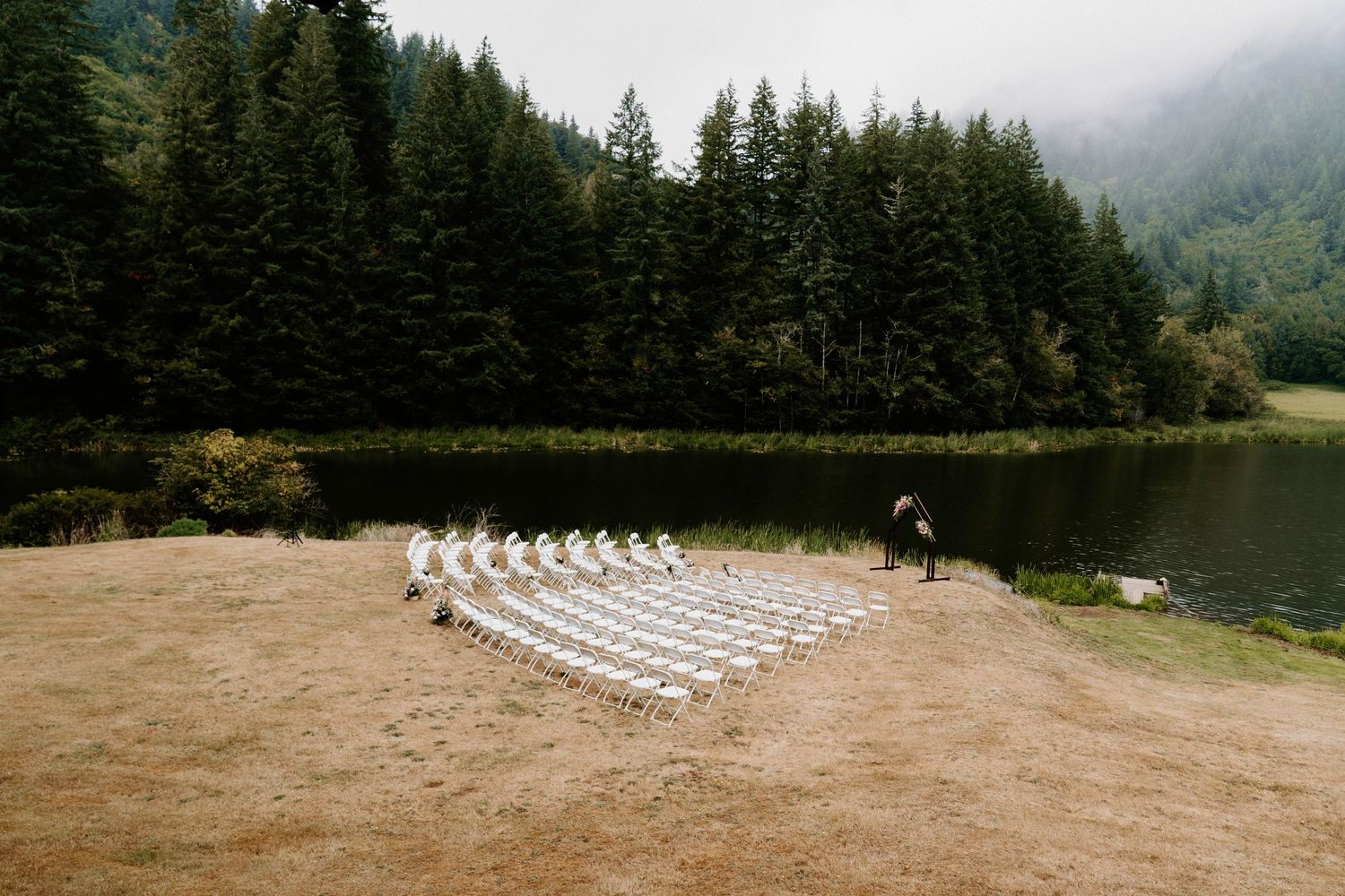 Outdoor wedding ceremony setup with white chairs against a backdrop of misty mountain forests.