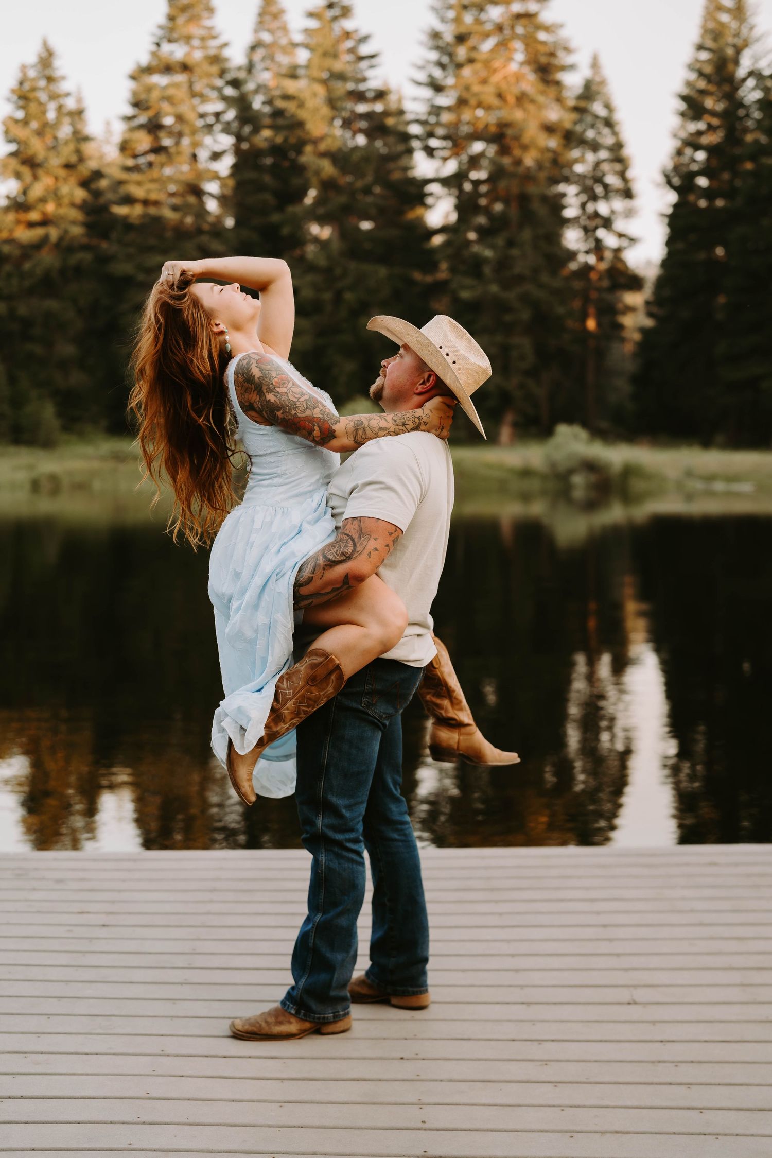A couple dances and spins on a wooden dock surrounded by a scenic lake and forest.
