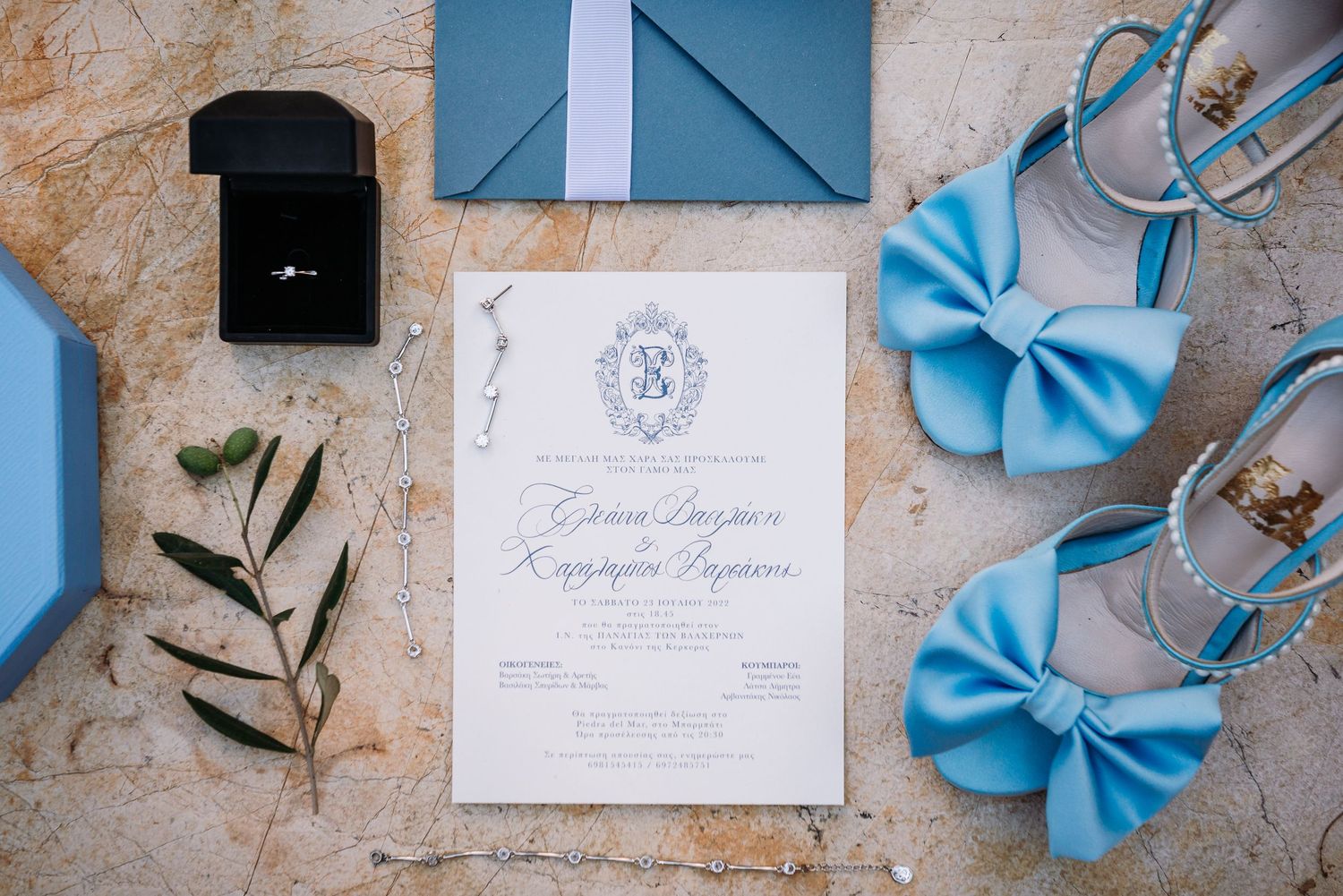 Wedding stationery and blue accessories arranged on textured stone surface.