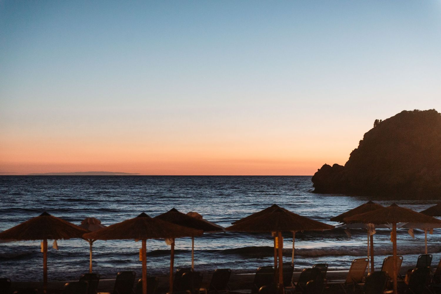 Beach umbrellas silhouetted against a colorful coastal sunset.