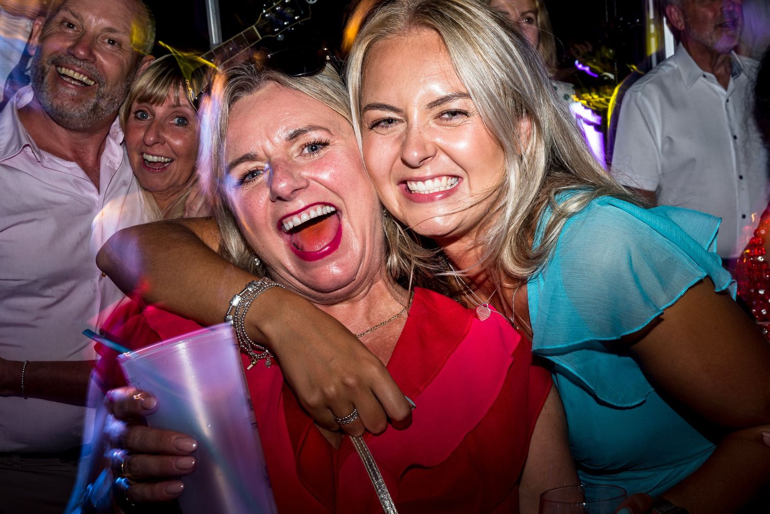 Guests laughing and celebrating in colorful party attire under vibrant lighting.