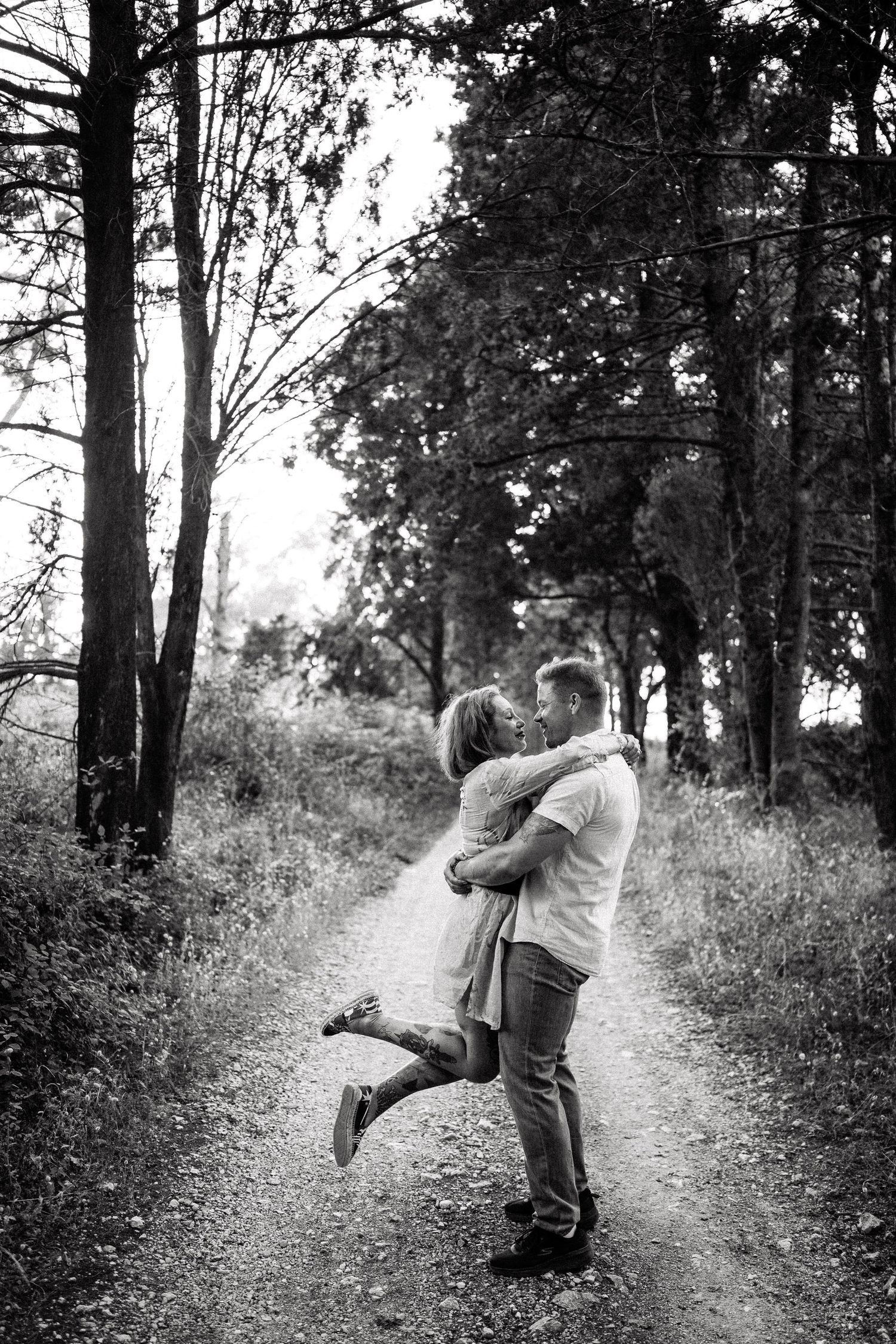 A romantic couple embraces on a wooded forest path during a photo session.