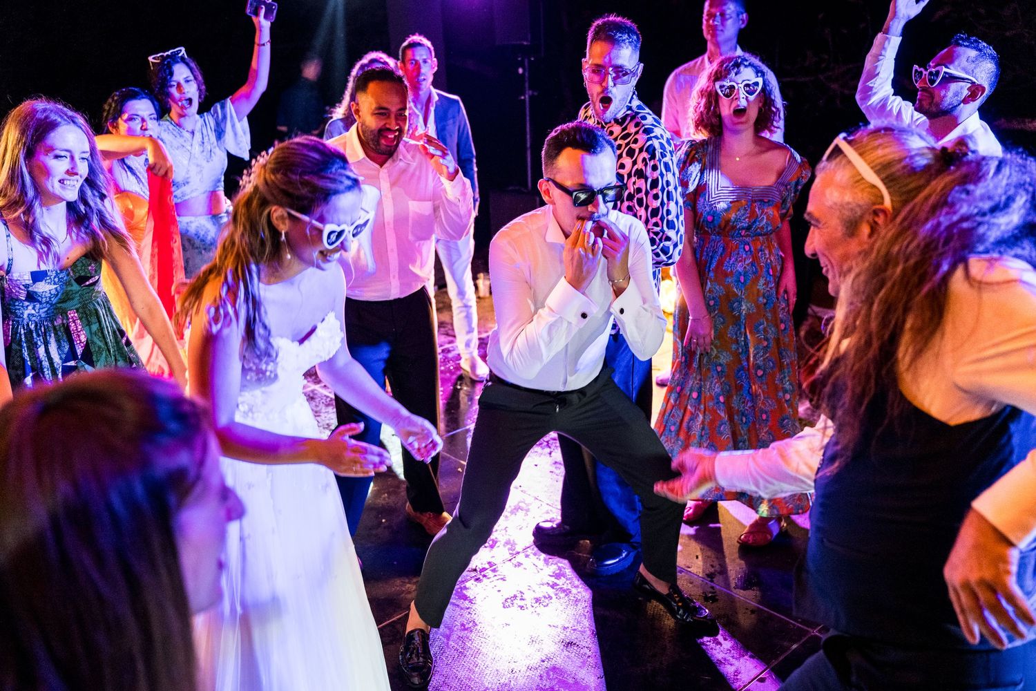 Energetic dance party scene with people moving under purple and pink lighting.